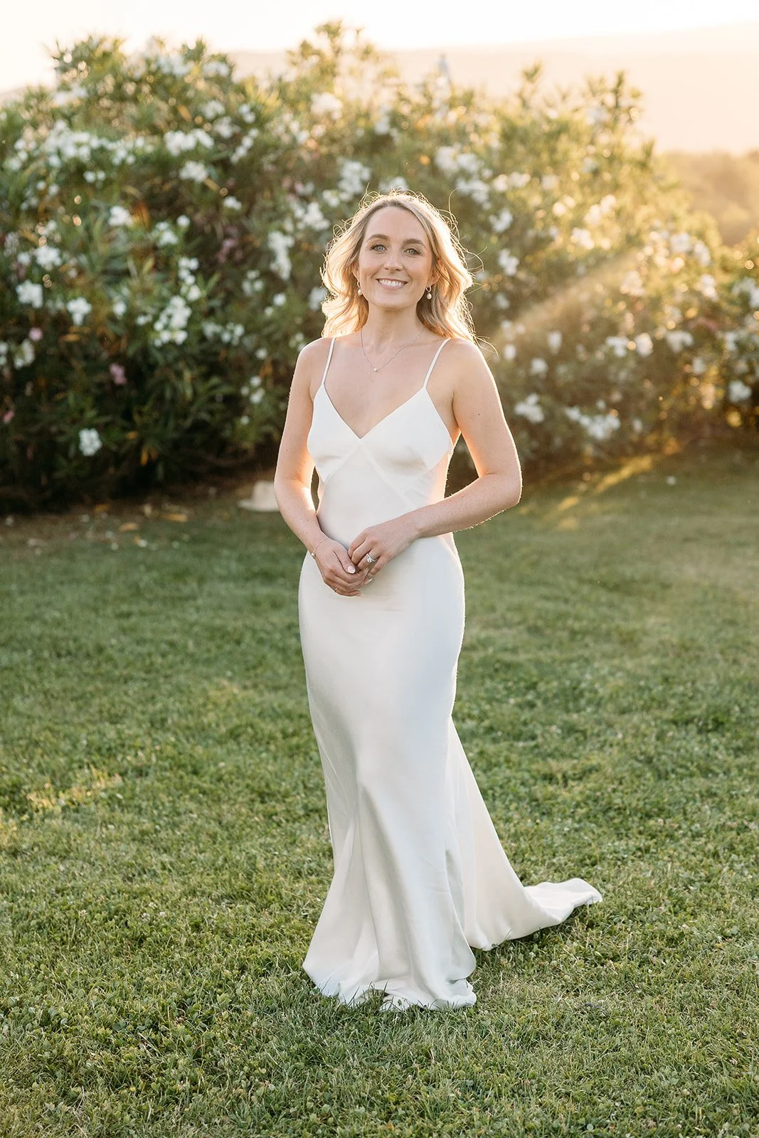 Bride in a silk slip gown in the garden at golden hour in Provence, luminous natural wedding makeup by Mathilde Vintze