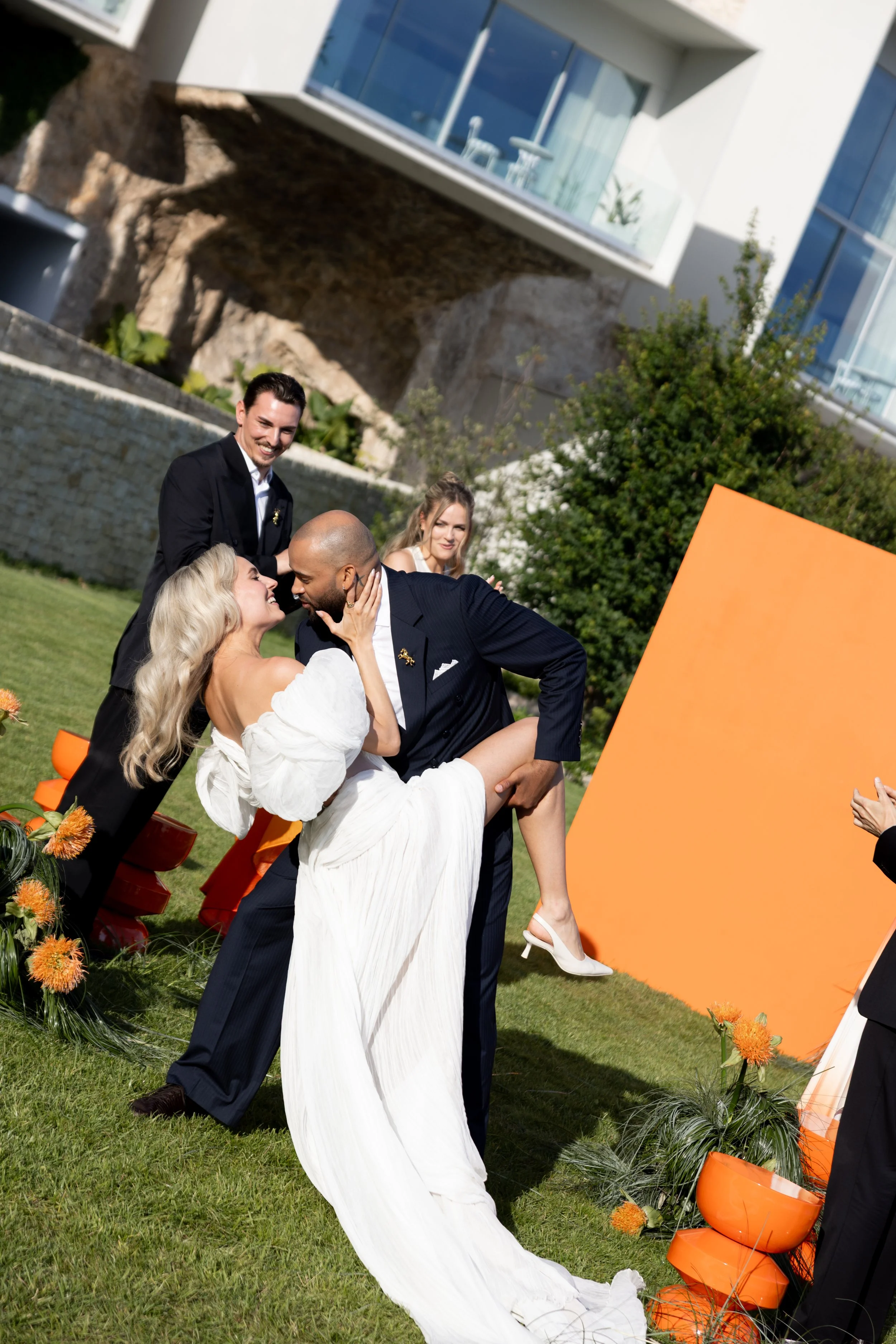 Groom dipping the bride for a kiss on the lawn in front of the orange ceremony backdrop at The Maybourne Riviera, wedding makeup by Mathilde Vintze