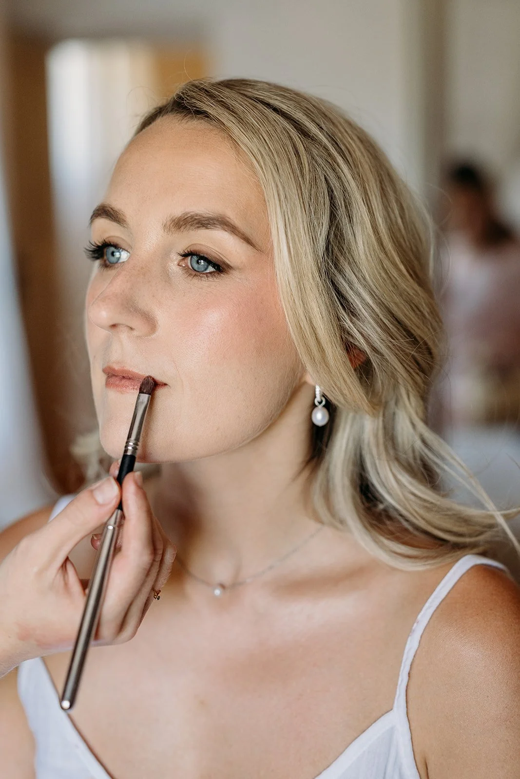 Close-up of the bride's lips being finished with a brush, soft nude tones and pearl earrings, bridal makeup in Provence by Mathilde Vintze