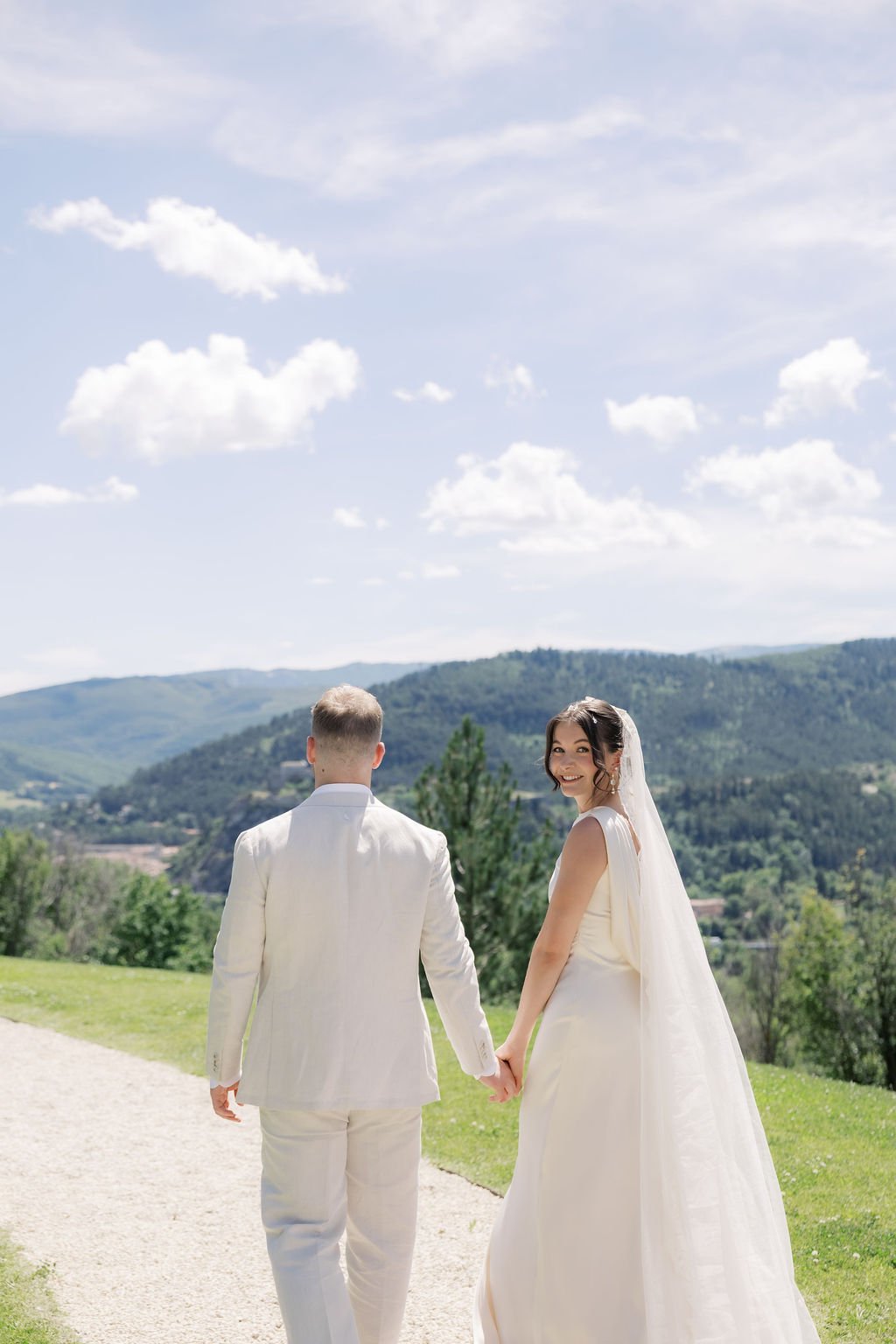Bride and groom walking a path with sweeping Provence hills behind them, timeless natural bridal makeup by Mathilde Vintze