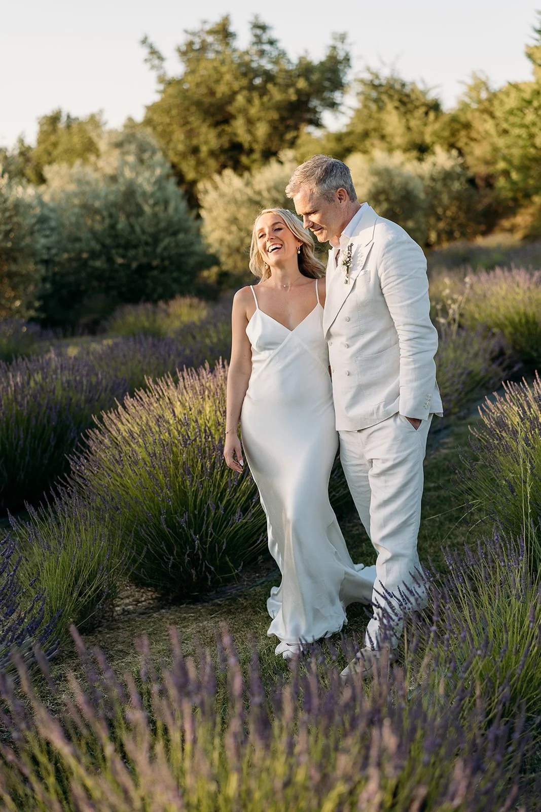 Bride and groom walking through the lavender at golden hour at Le Clos du Tuillier, soft natural bridal makeup in Provence by Mathilde Vintze
