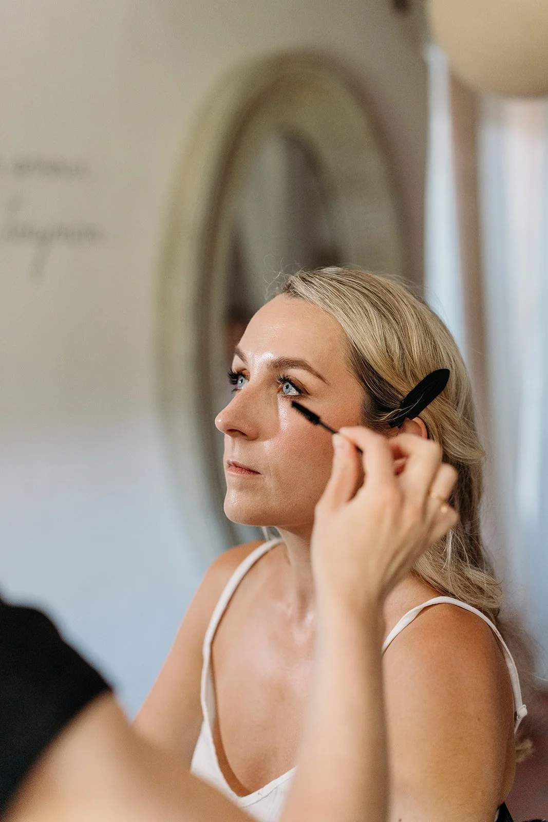 Close-up of the bride having her mascara applied at the mirror, soft glowing skin, bridal makeup in Provence by Mathilde Vintze