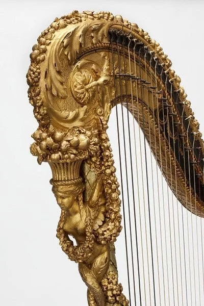 Pala de un arpa dorada con detalles decorativos elaborados y figuras escultóricas