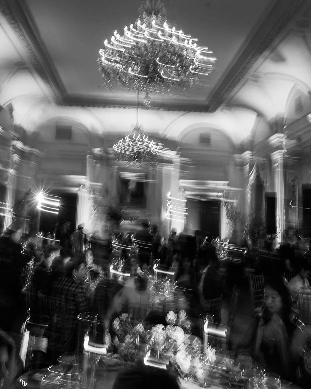 Sala de eventos elegante con candelabros y mesas con flores, en colores en blanco y negro, imagen desenfocada.