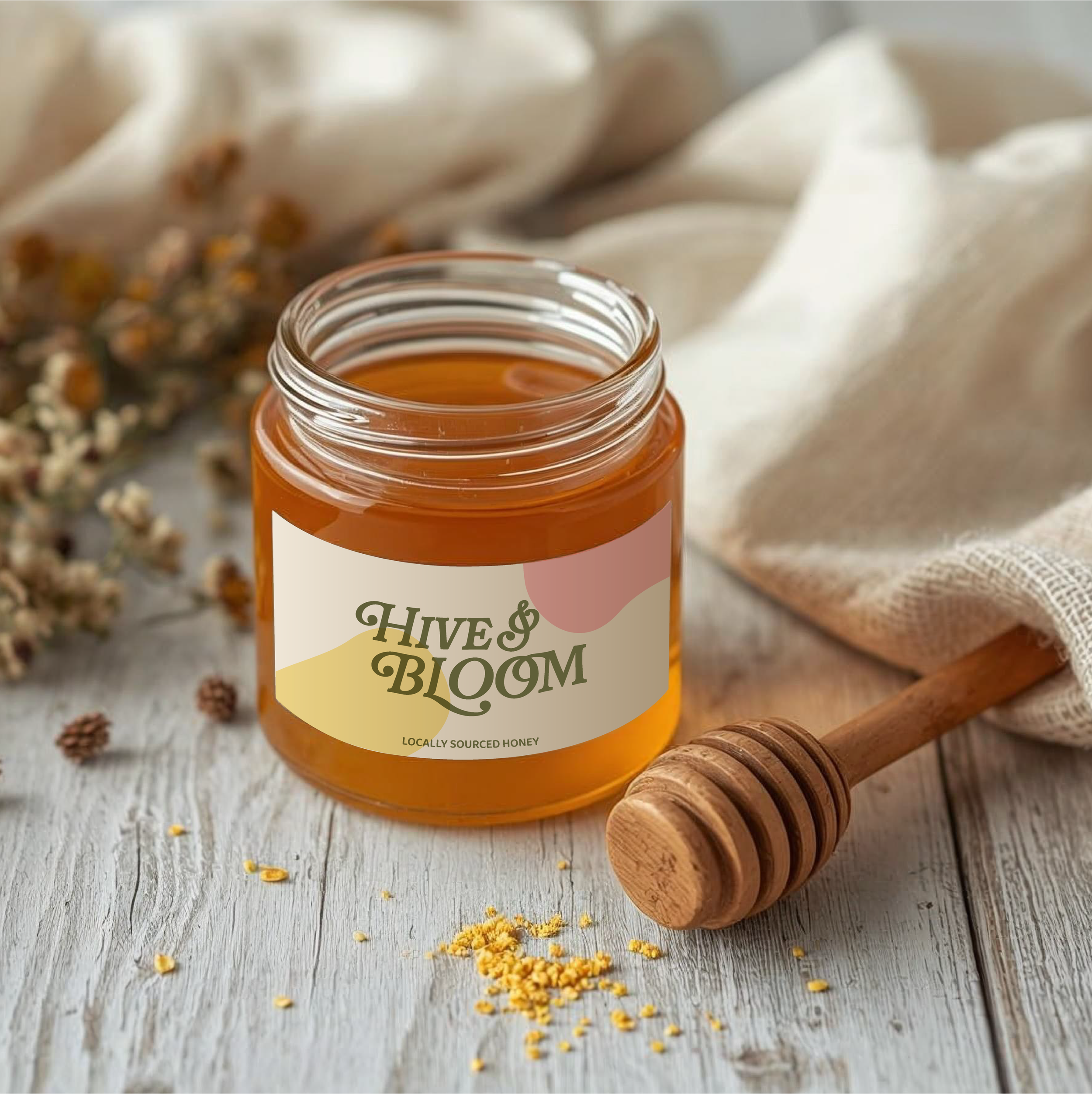 A jar of honey labeled "Hive & Bloom" with a honey dipper placed beside it on a rustic wooden surface, with some flower and honey granules scattered around.