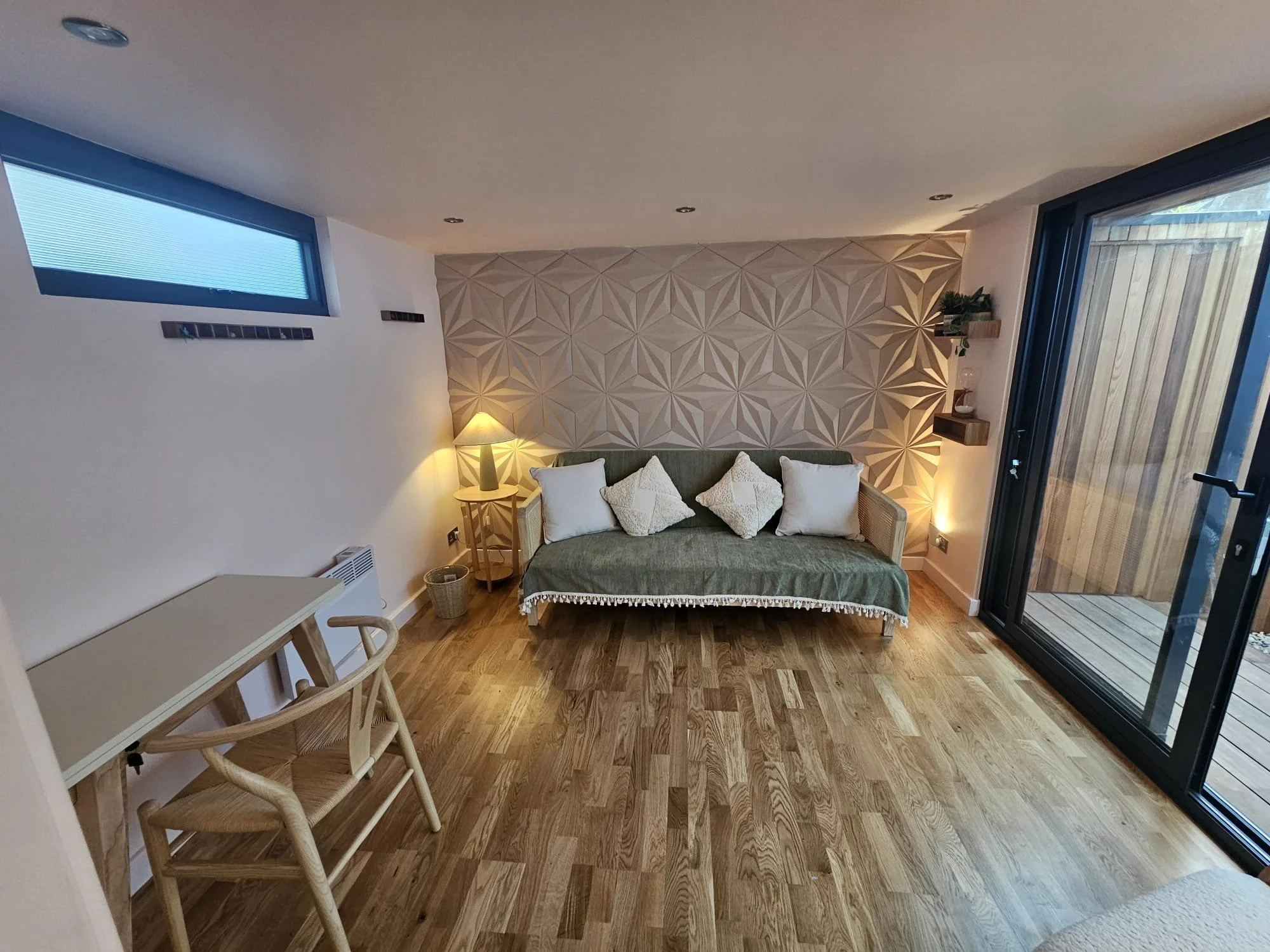 Living room with a couch, pillows, a lamp, a small desk and chair, and a sliding glass door leading outside.