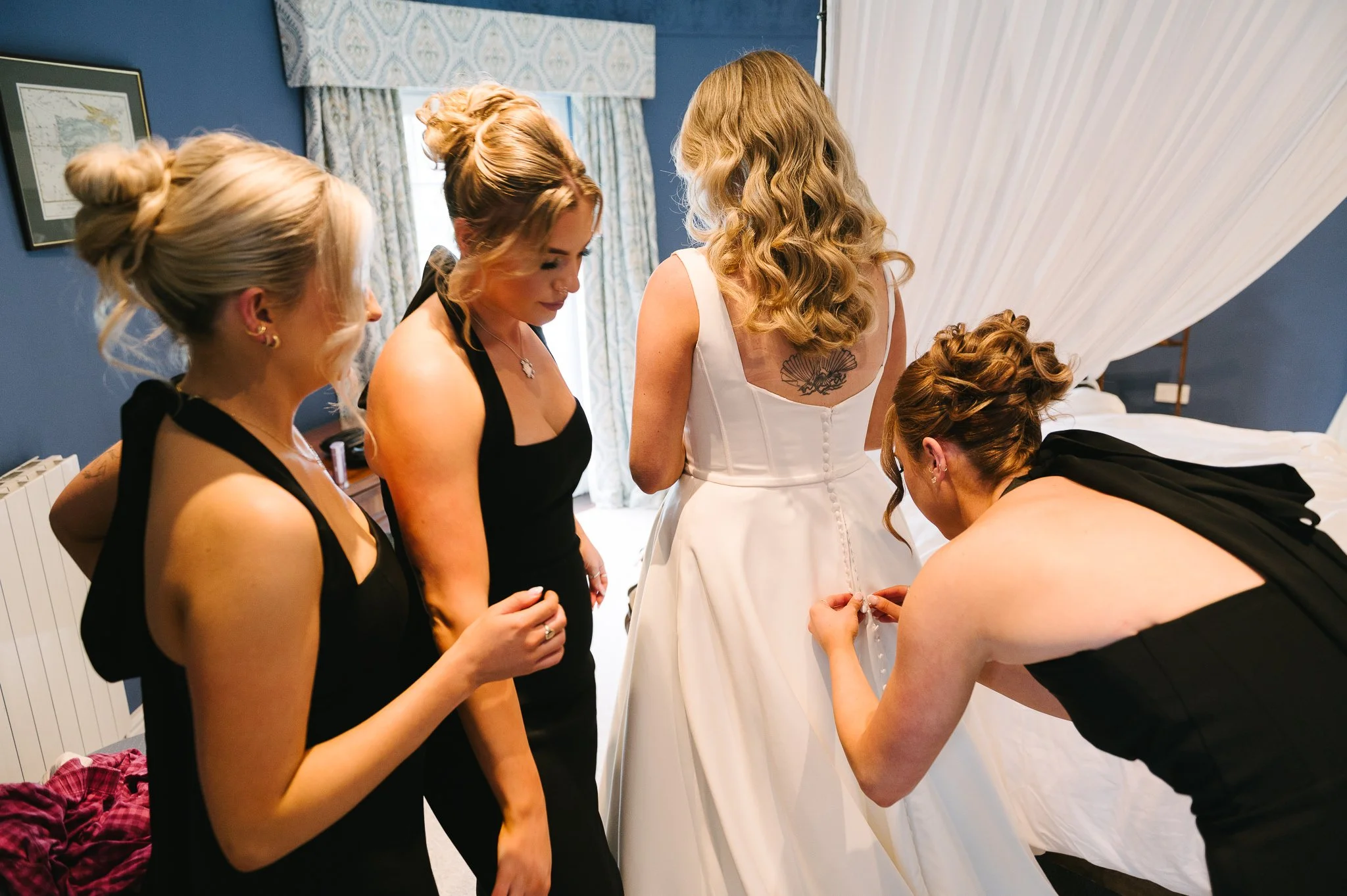 Bridesmaids fastening the brides dress