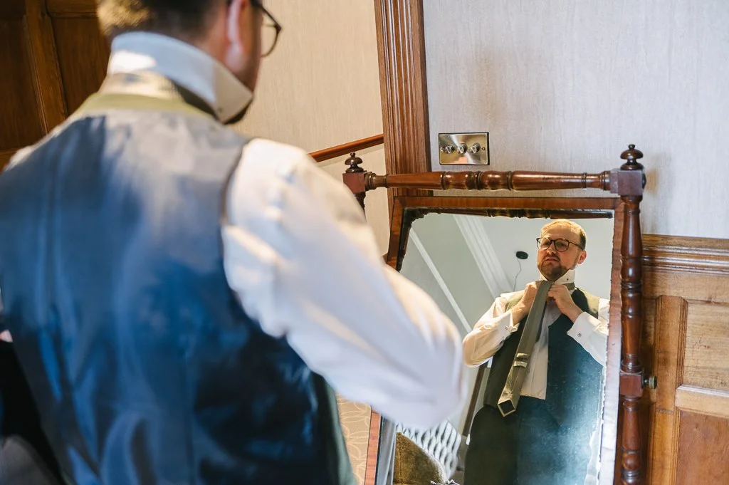 Groom fastening his tie in the mirror