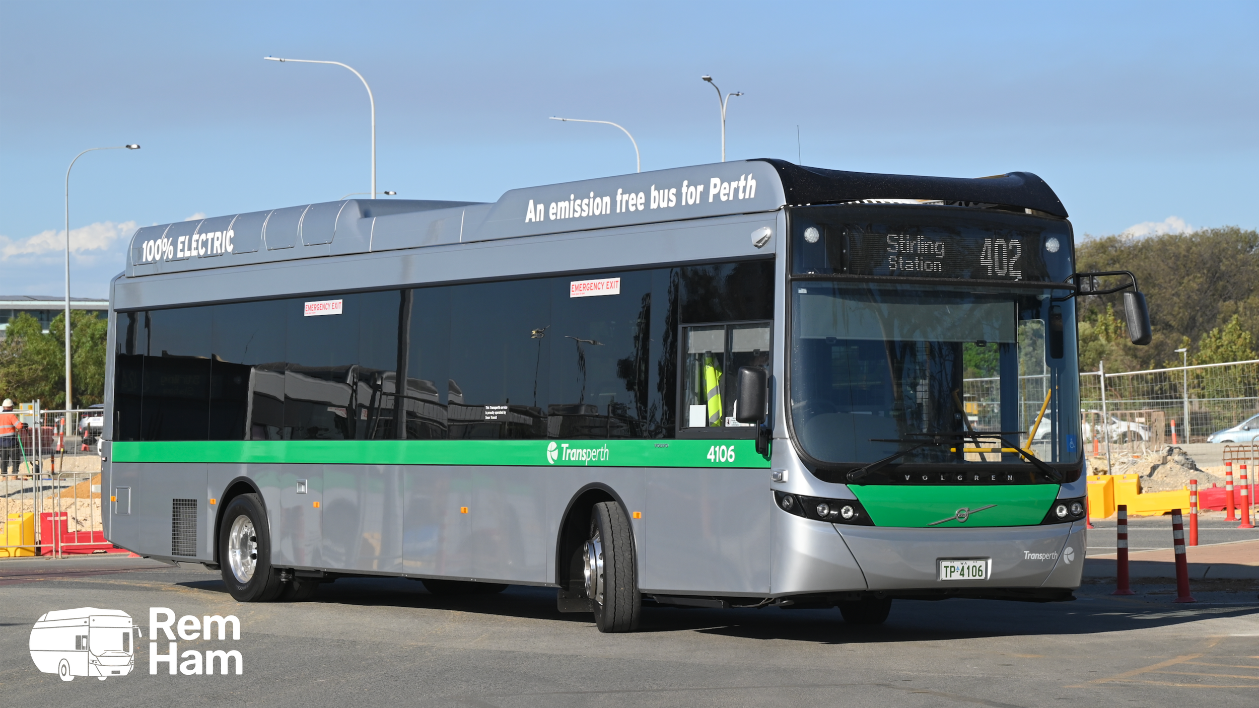 A silver and green electric bus labeled 'Transperth' parked at a bus station with construction in the background.