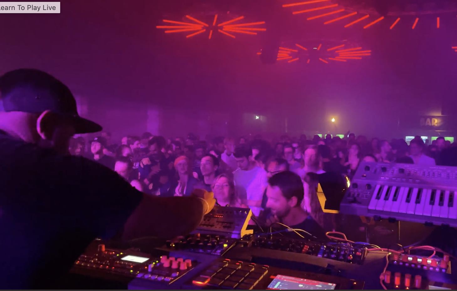 Analog Kitchen live performing at a nightclub with a crowd dancing, colorful lights, and electronic music equipment.