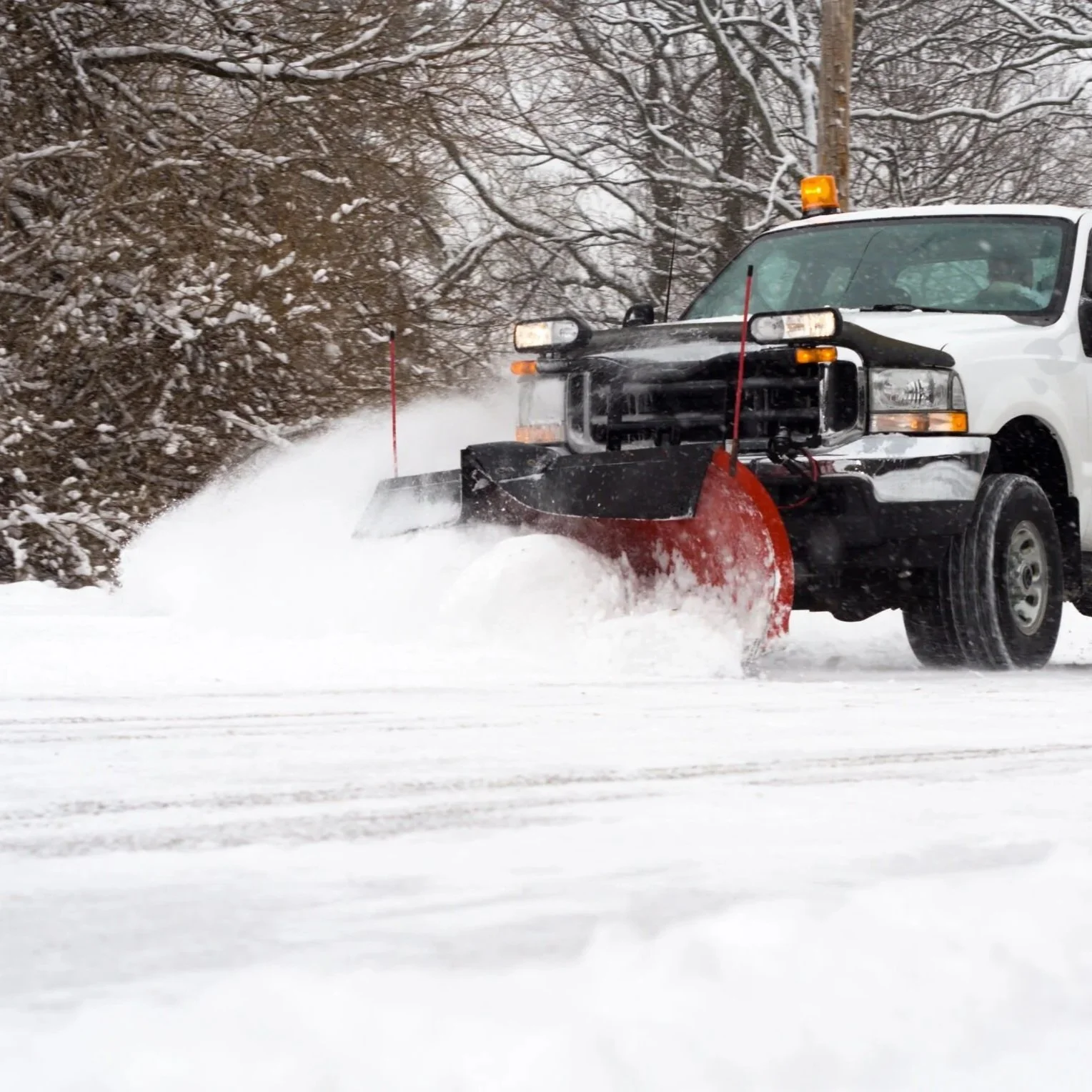 A white utility truck with a snow plow clearing snow from a road during winter.