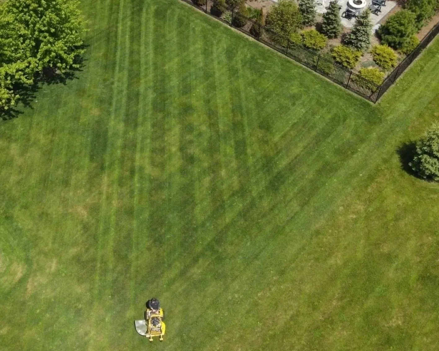 Large green lawn being mowed by a yellow riding mower with a black operator.