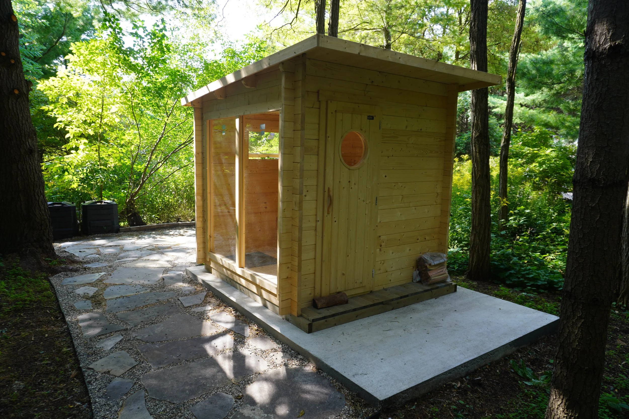 Small wooden cabin or shed in a forested area with a stone pathway.