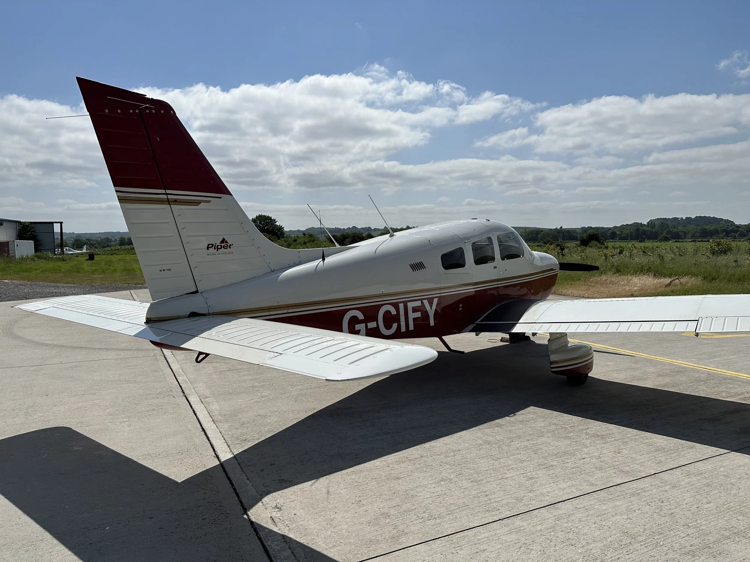 PA28 G-CIFY, Small Piper aircraft parked on a tarmac with grassy landscape and cloudy sky in the background.