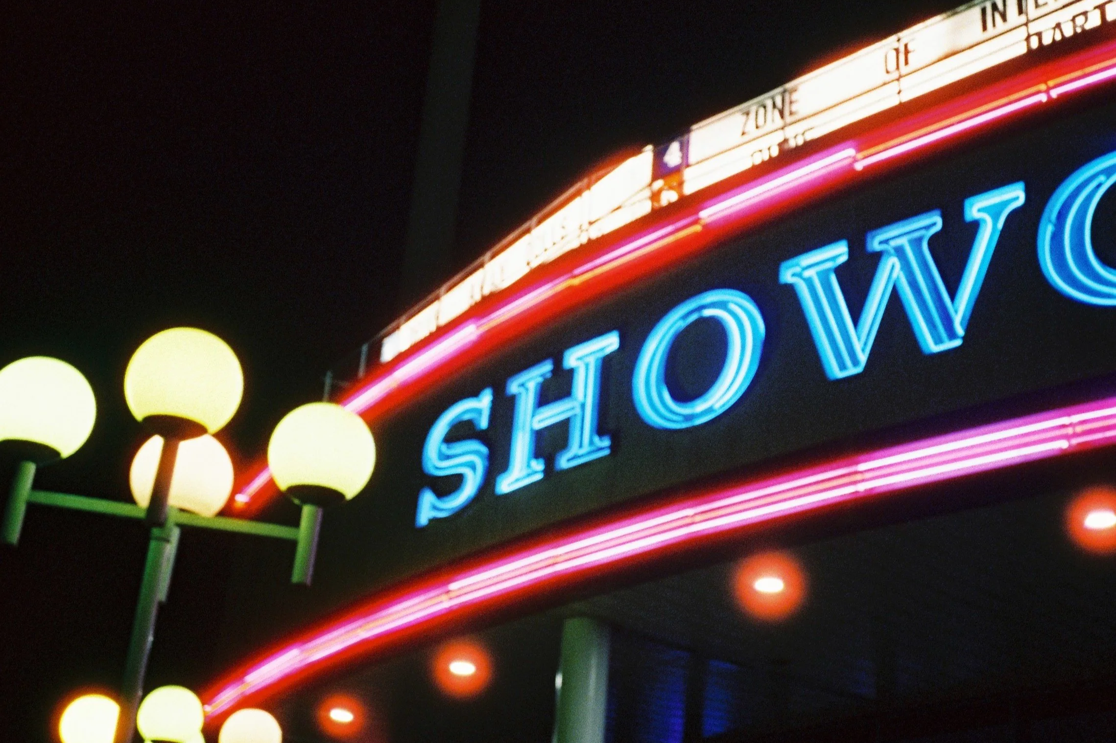 Neon sign saying "SHOWN" at night, with decorative street lamps nearby.