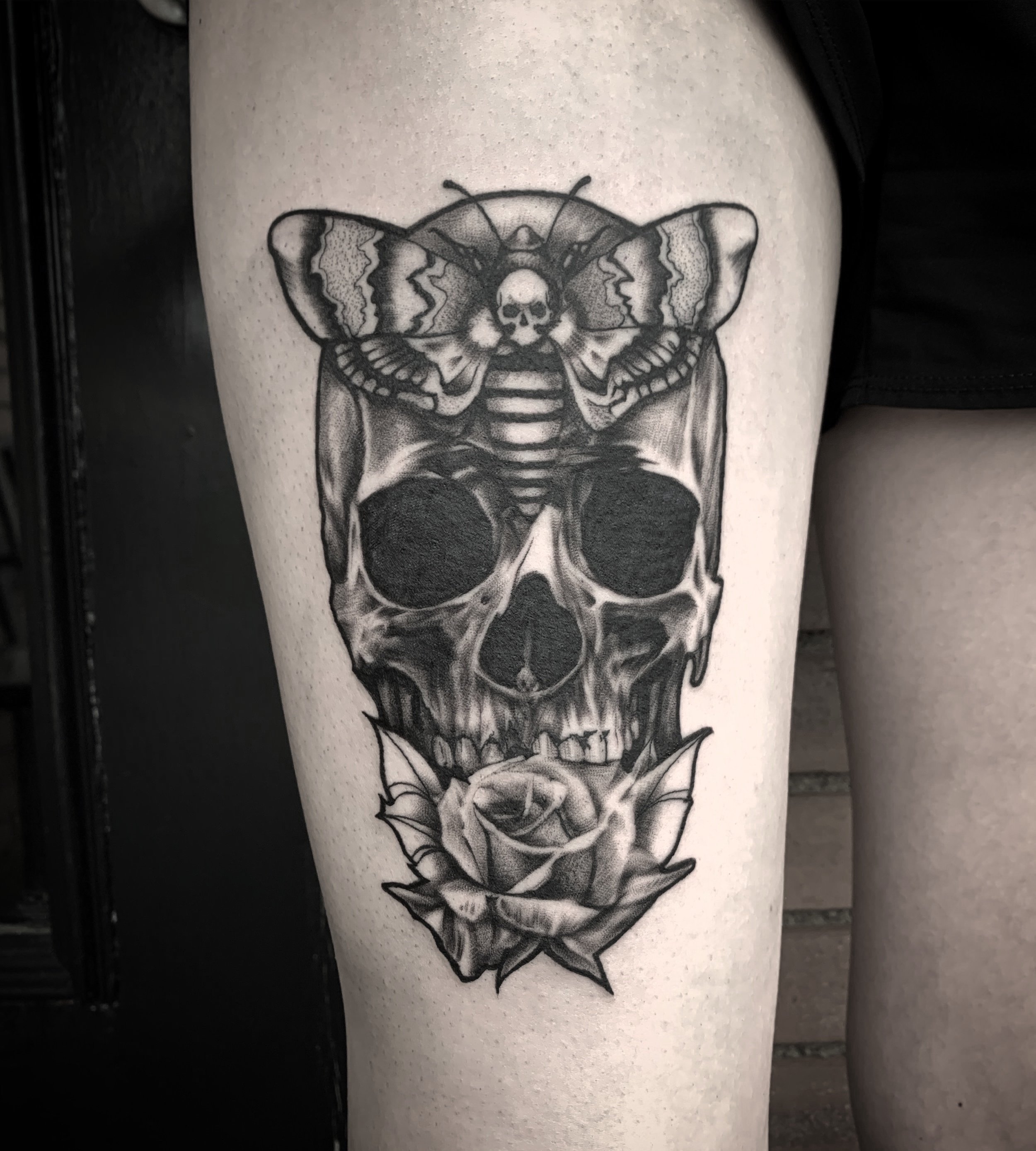 Black and gray tattoo of a skull with a rose in its mouth, a bee with wings spread and a skull face on top of the skull, and a small skull face on the bee's body. Tattoo, tattoo artist, tattoos, realistic tattoo, portrait tattoo, artistic tattoo, exp