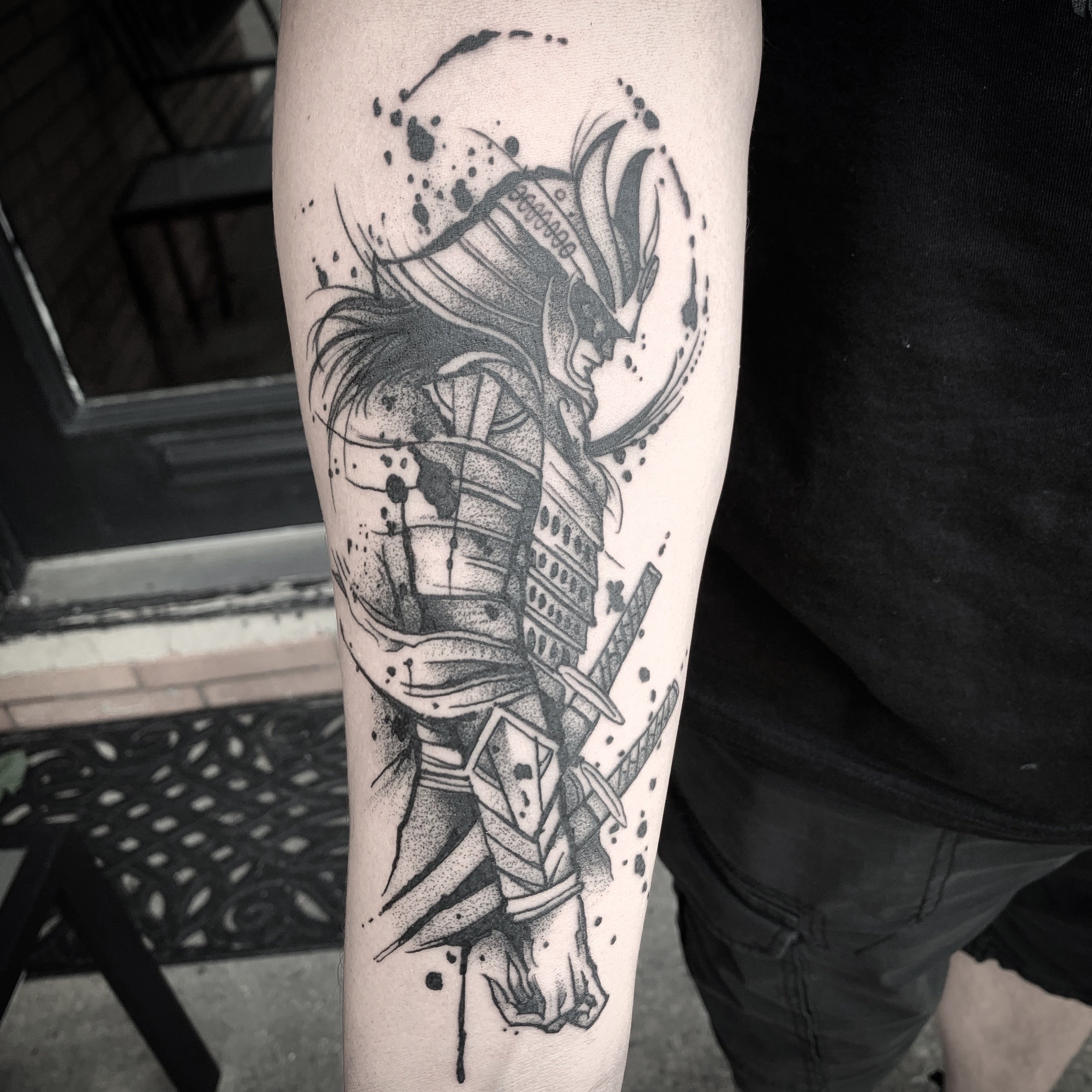 Black ink tattoo of a fierce warrior with a detailed helmet and armor, holding a large sword, surrounded by splashes and abstract designs. Tattoo, tattoo artist, tattoos, realistic tattoo, portrait tattoo, artistic tattoo, experienced tattoo artist,