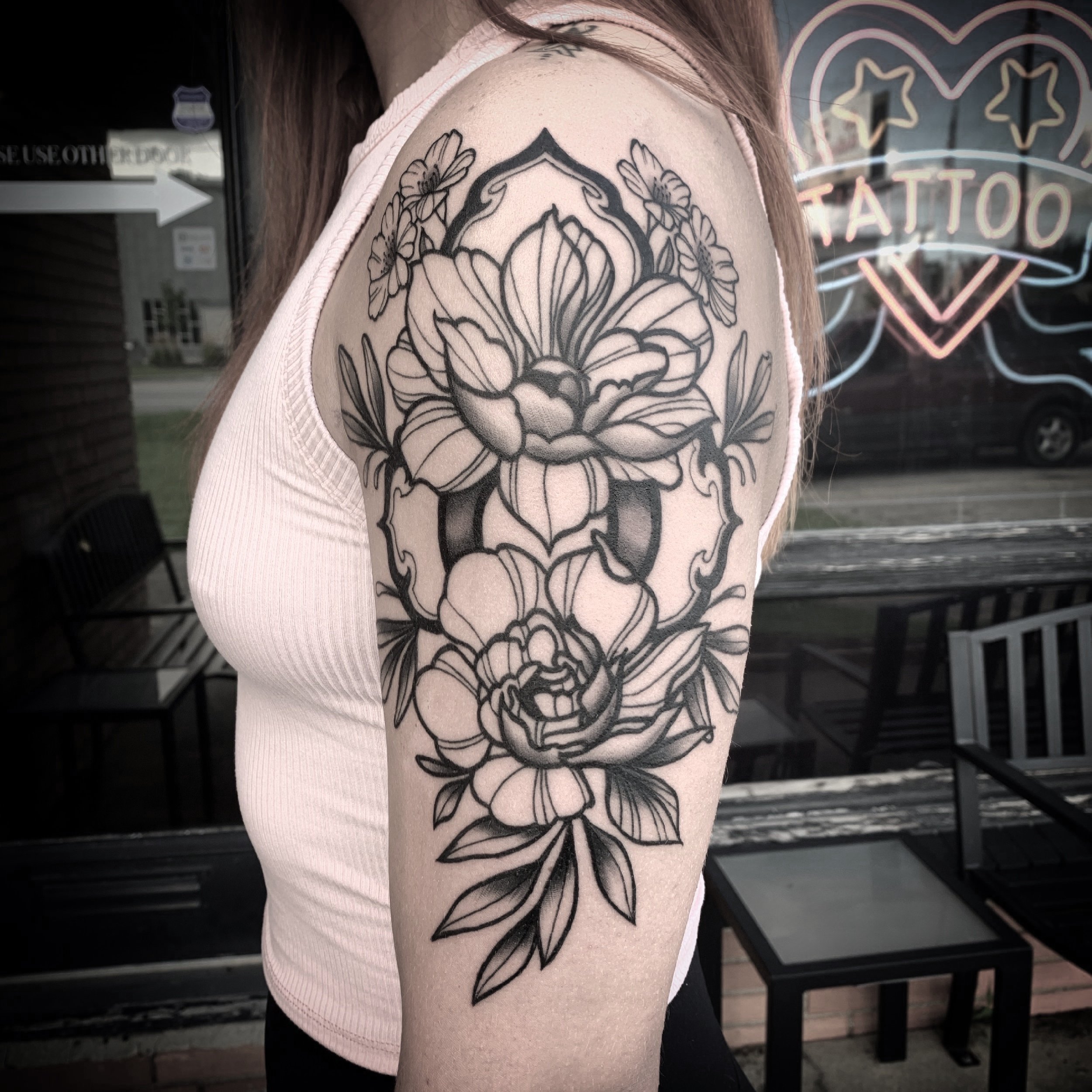 A black and gray floral tattoo on a person's upper arm, featuring large blooming flowers and leaves. Tattoo, tattoo artist, tattoos, realistic tattoo, portrait tattoo, artistic tattoo, experienced tattoo artist, Oregon, tattoo artist near me, nature