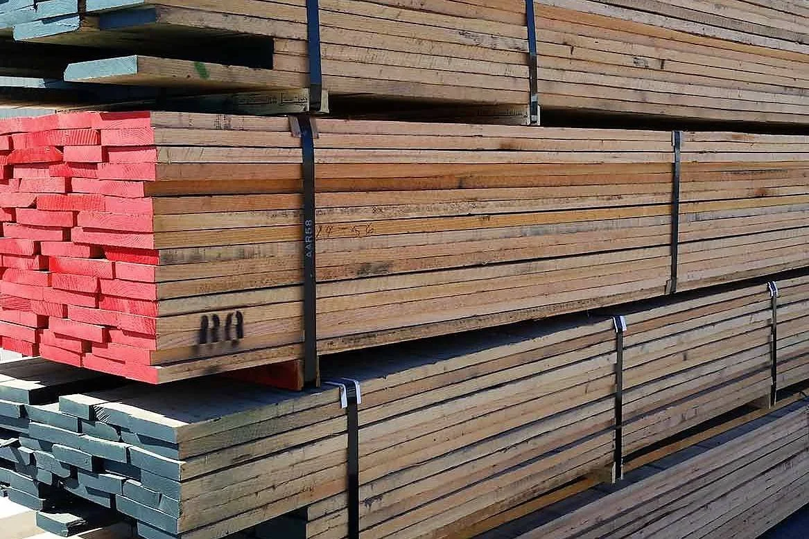 Stacks of wooden planks in different sizes and colors, tied together with metal straps in an outdoor lumber yard.