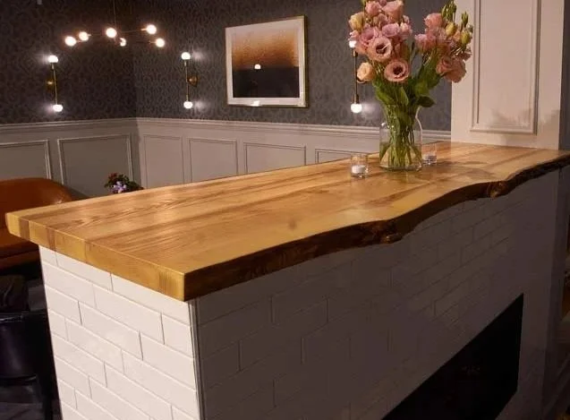 A kitchen or dining area with a wooden countertop, white brick base, vase of pink flowers, and artwork on the wall.