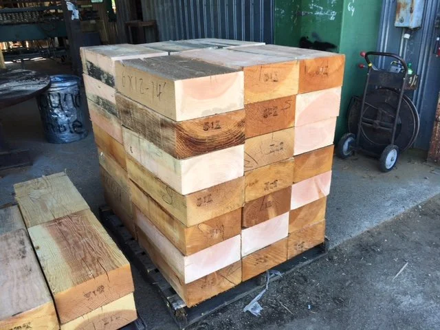 Stack of large wooden beams arranged in a cube on a pallet in a workshop or warehouse.