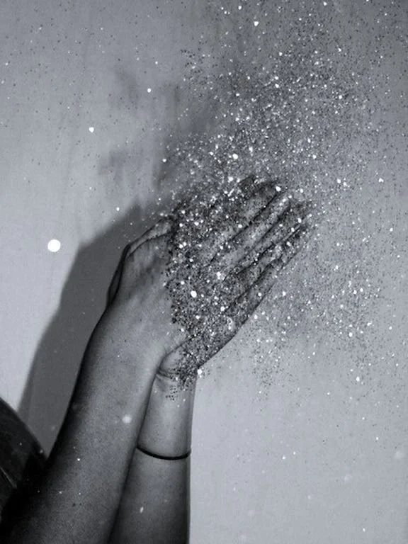 Person clapping their hands, causing silver glitter to scatter into the air.