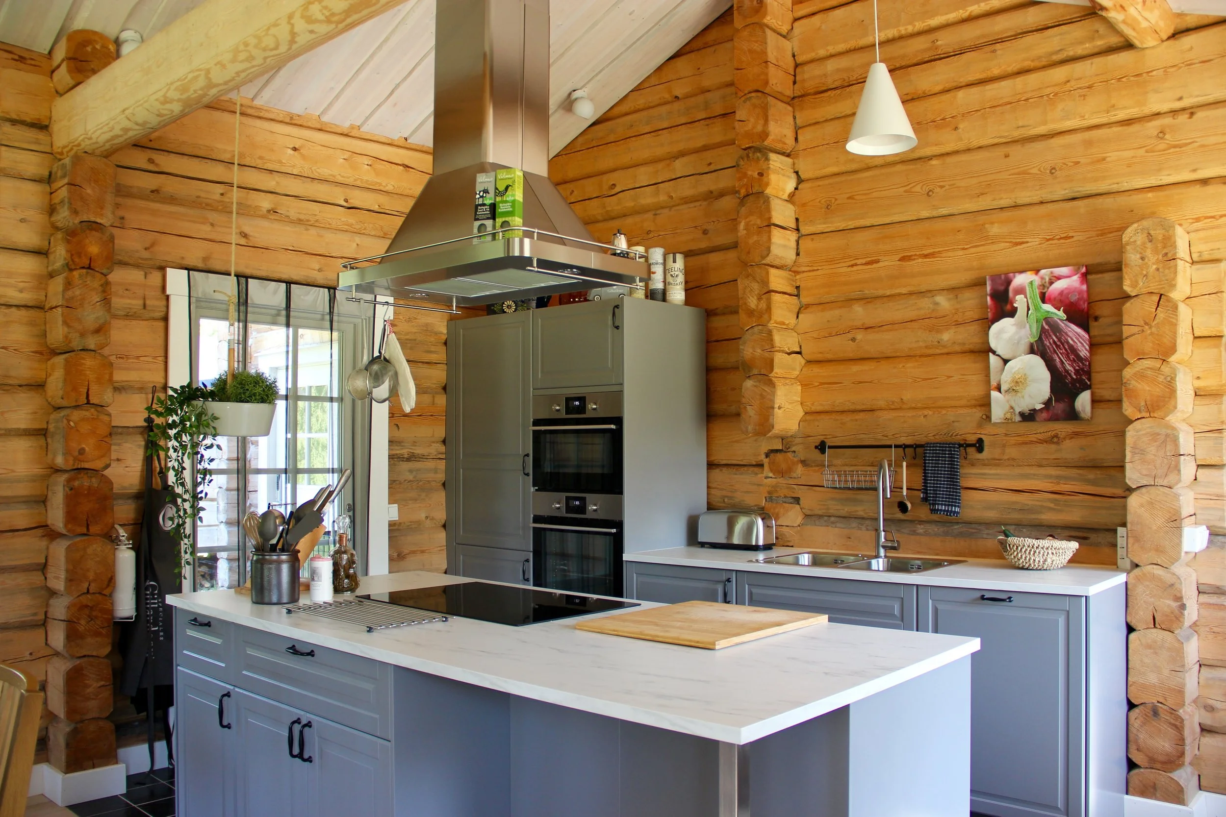 Kitchen with wood panel walls, gray cabinets, white marble countertop island, built-in oven and microwave, stainless steel range hood, and various kitchen items.