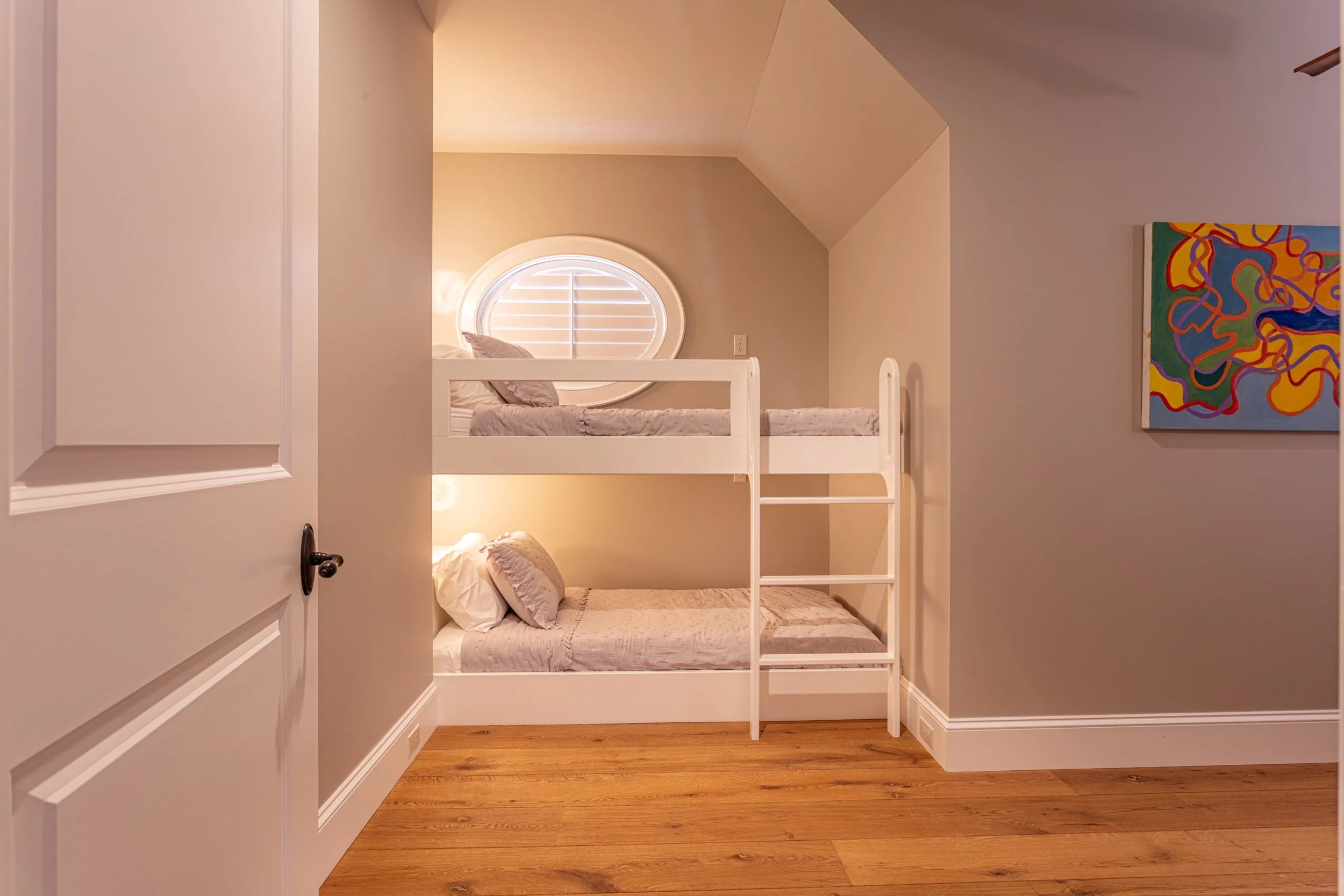Small bedroom with modern bunk beds, round window, and abstract wall art