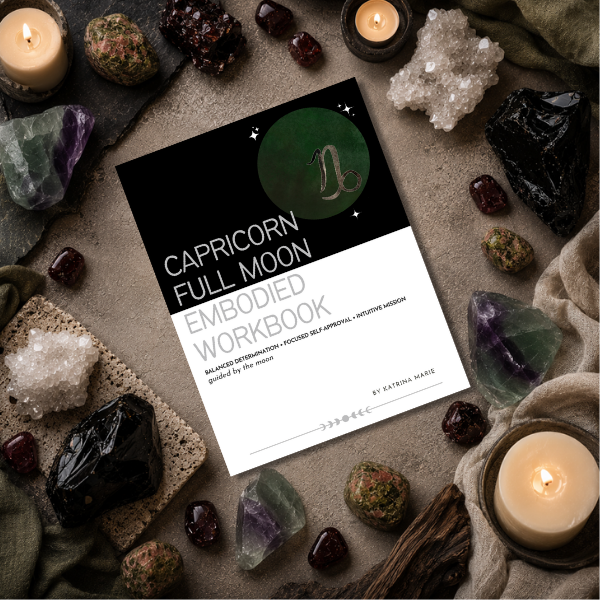 The Capricorn Full Moon Embodied Workbook cover displayed on a dark stone surface surrounded by crystals and lit candles, balanced determination, focused self-approval, and intuitive mission, guided by the moon, by Katrina Marie