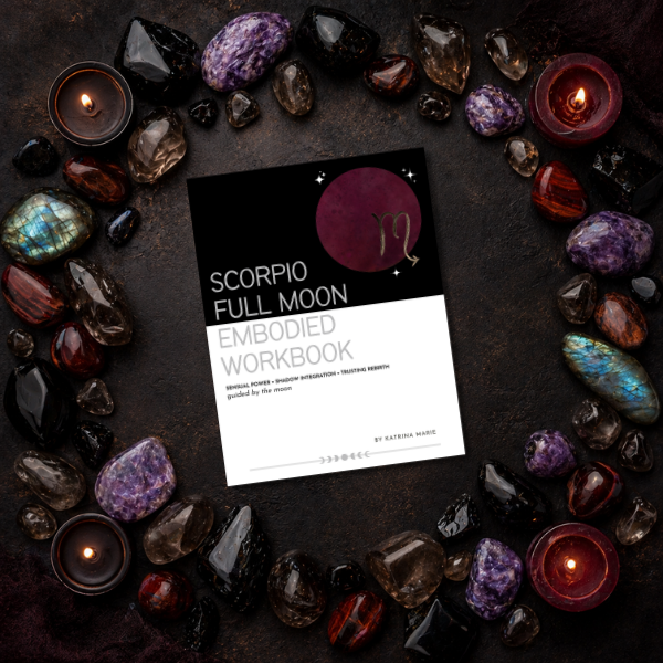 Scorpio Full Moon Embodied Workbook cover displayed on a dark stone surface surrounded by crystals and lit candles — sensual power, shadow integration, trusting rebirth, guided by the moon, by Katrina Marie.