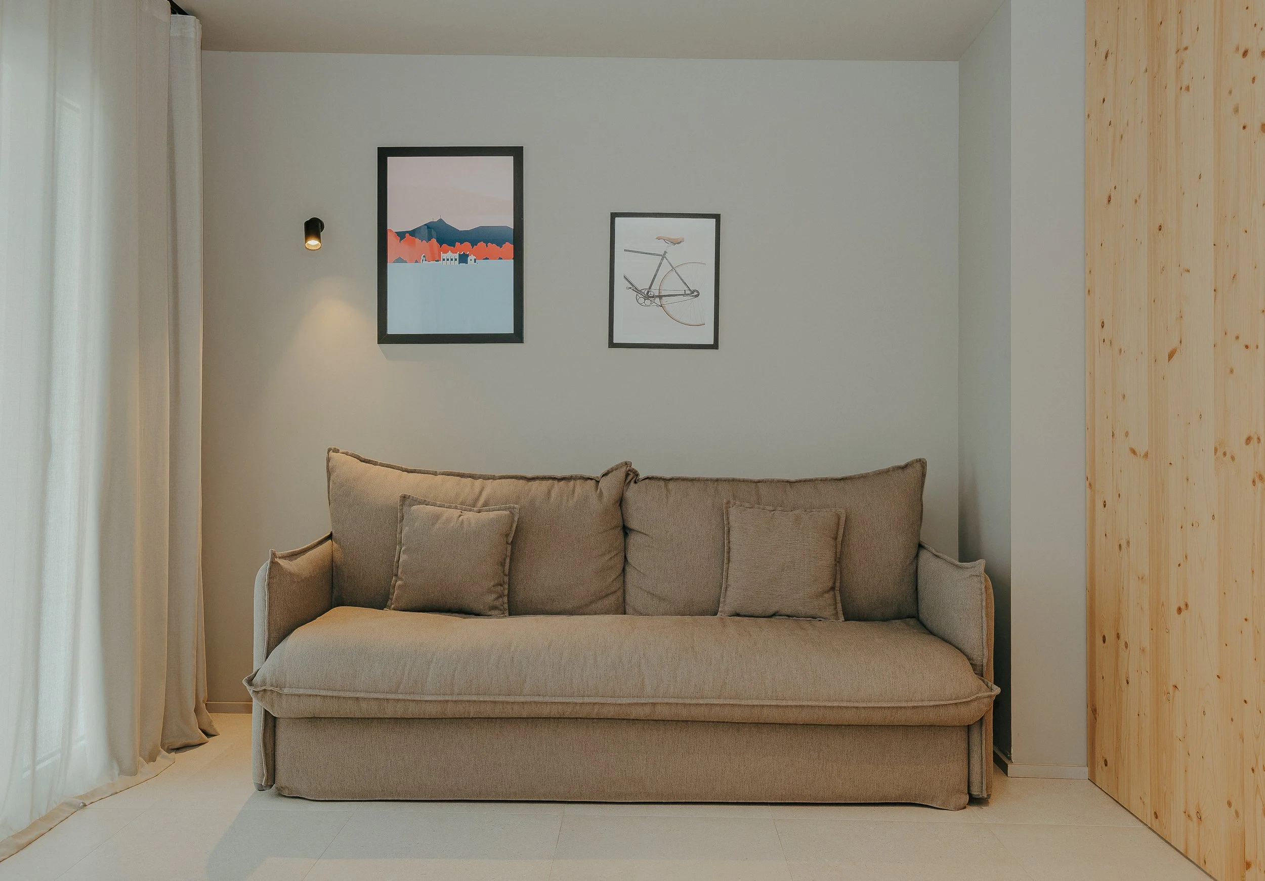 Sala de estar con sillón beige, tres cojines, cuadros en la pared y una pared de madera.