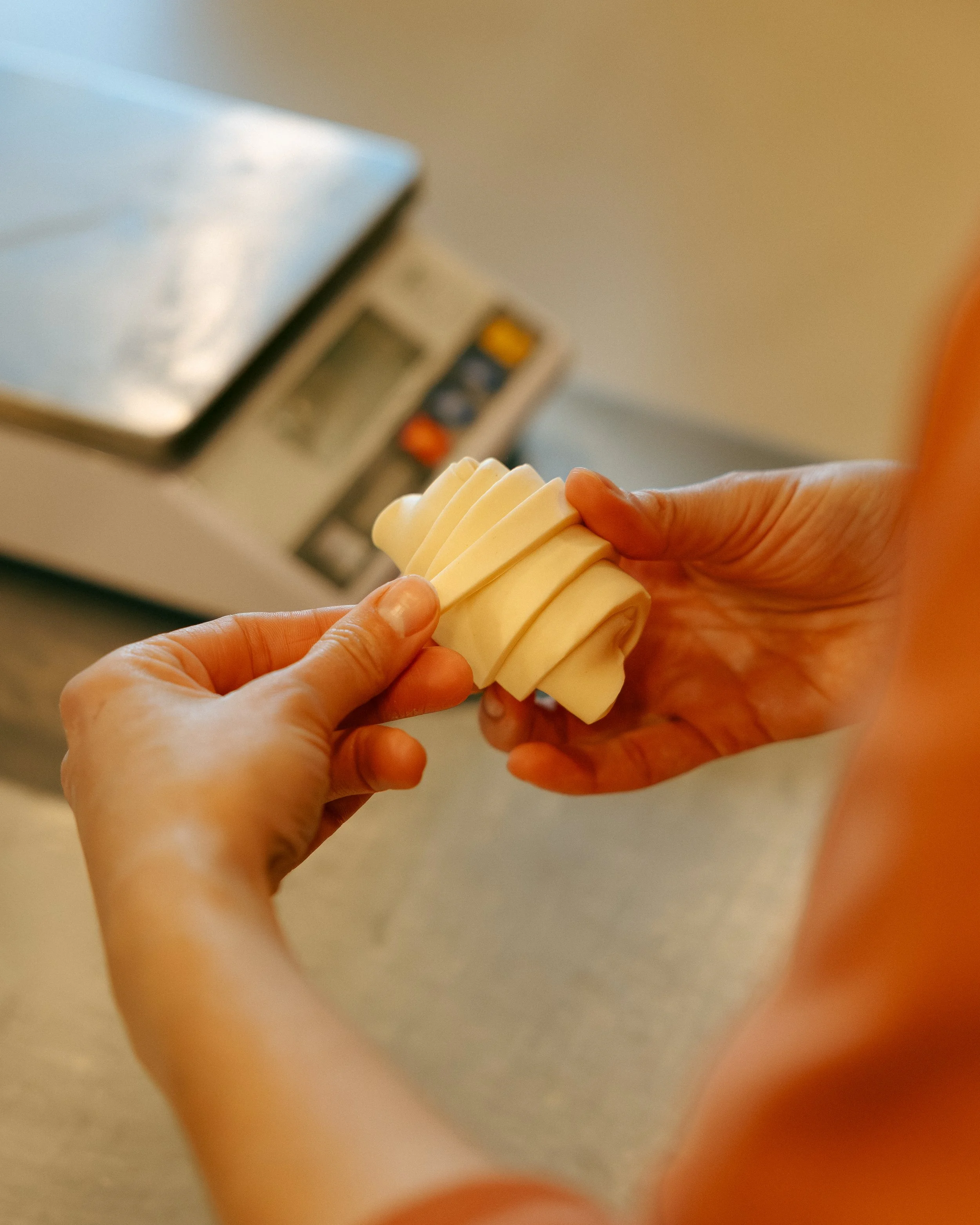 Persona trabajando con queso, cortándolo en láminas finas, en un ambiente de cocina o fábrica de alimentos.