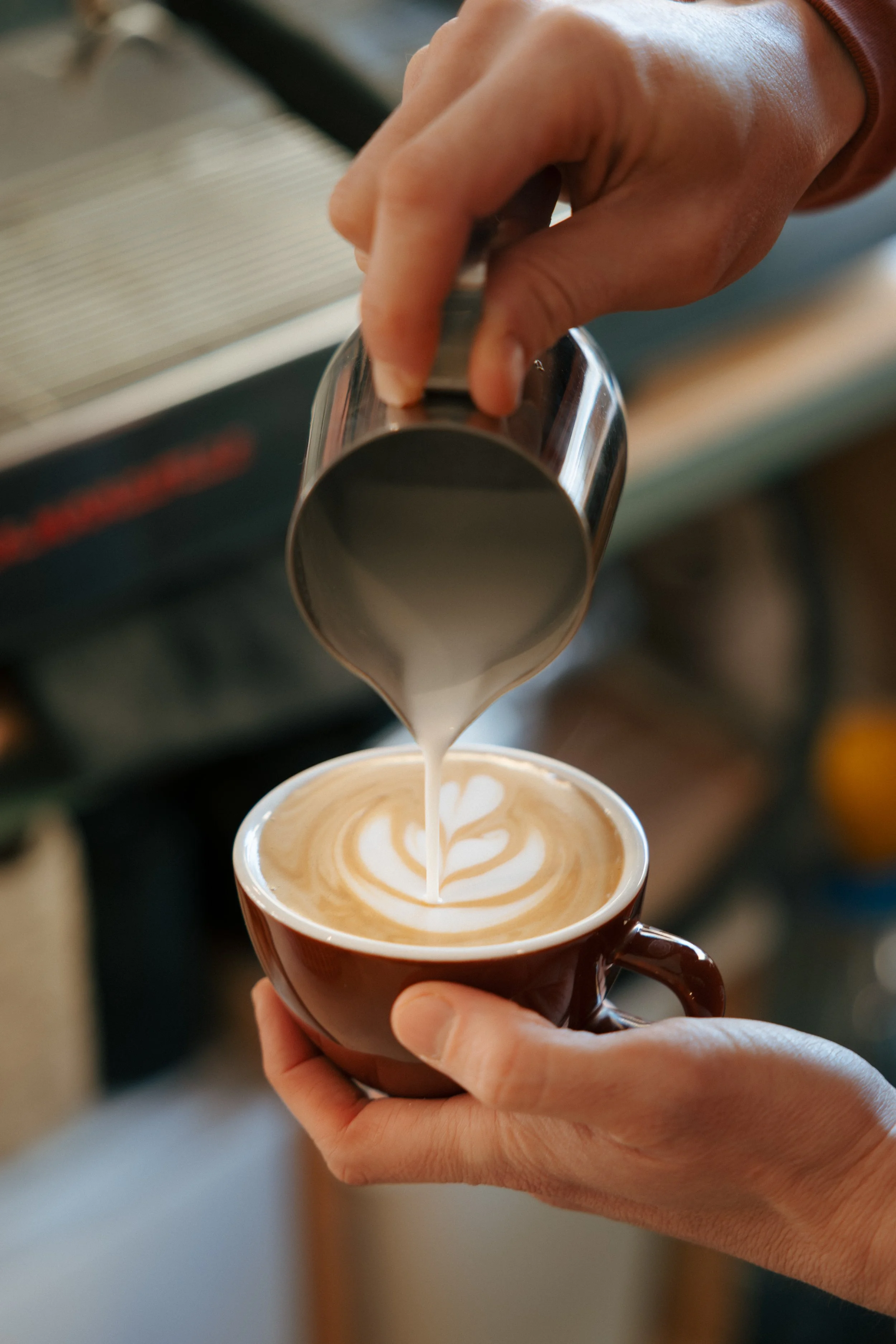 Persona sirviendo leche de vapor en una taza de café, creando arte latte.