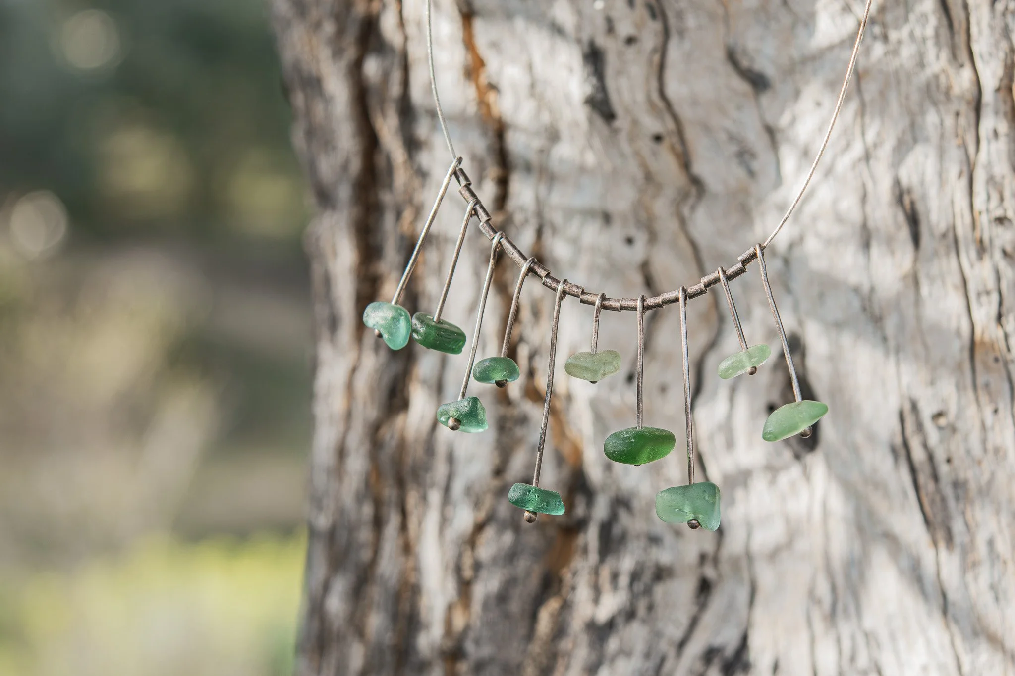 Collar de hilo con piedras verdes colgado en un árbol.