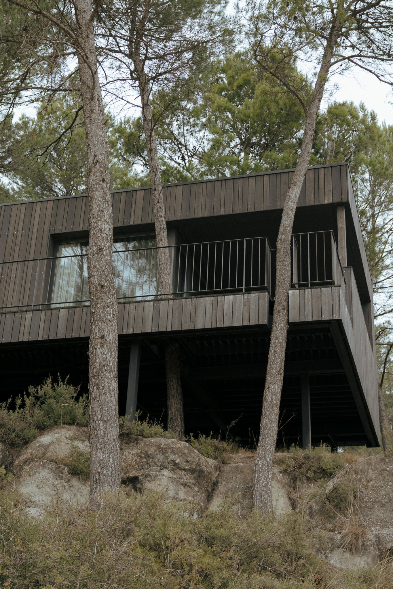 Casa moderna de madera elevada en un acantilado con árboles y rocas en primer plano.