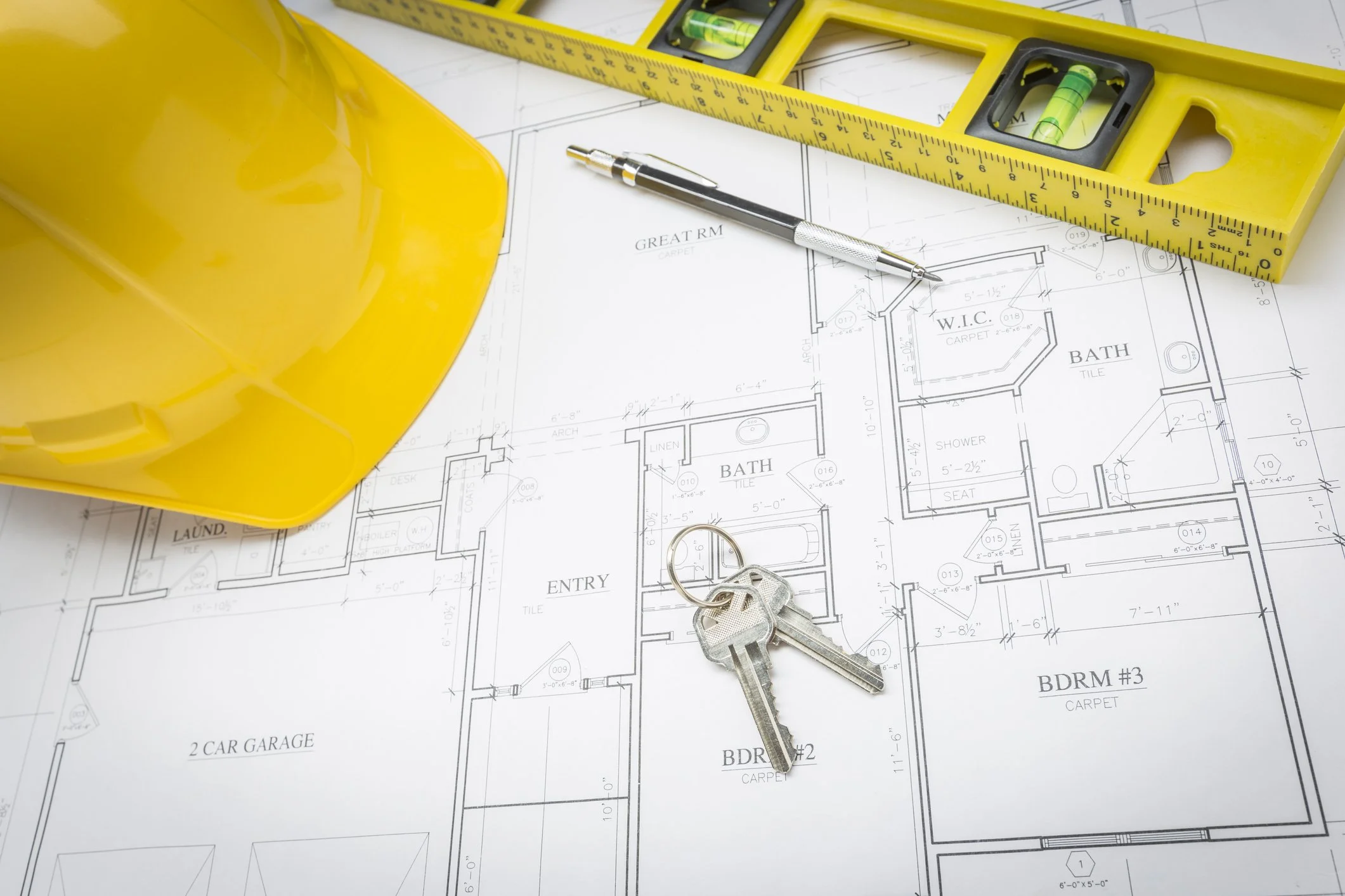 Construction blueprint with a yellow safety helmet, a spirit level, a measuring tape, a mechanical pencil, and a set of keys