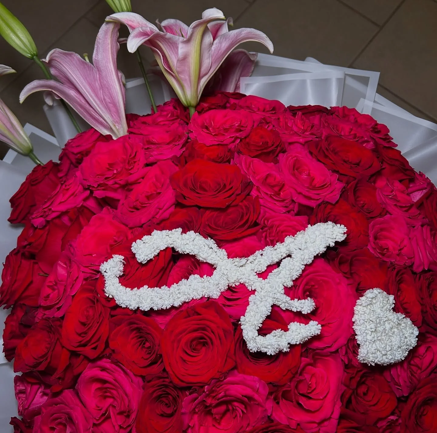 50 red roses, 50 hot pink roses + star fighter lilies wrapped in frosted white paper with a white border❤️🩷a pretty cursive A + lil heart made of fake baby&rsquo;s breath🤍