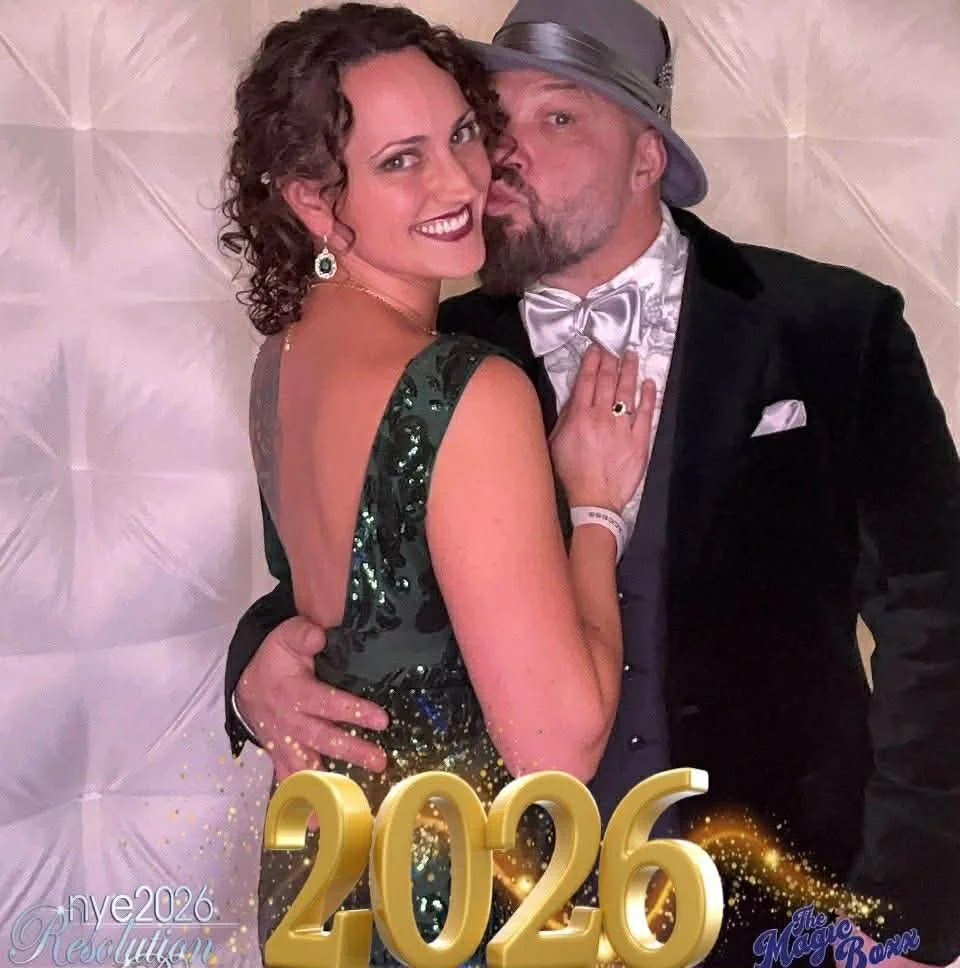 A couple dressed in formal attire celebrating at a 2026 New Year's event, with the date '2026' displayed in large gold numbers at the bottom.