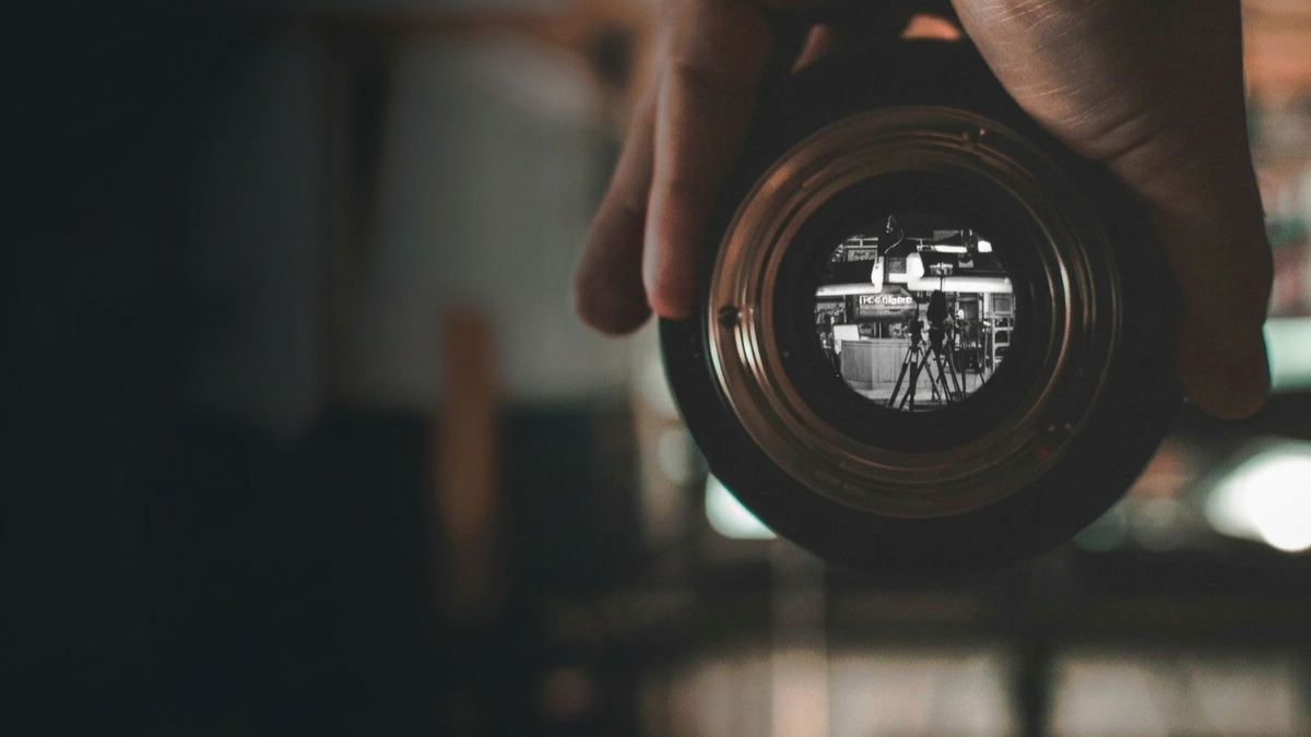 Close-up of a camera lens reflecting a media TV film studio scene on the EthicsVision workplace investigations and training homepage.
