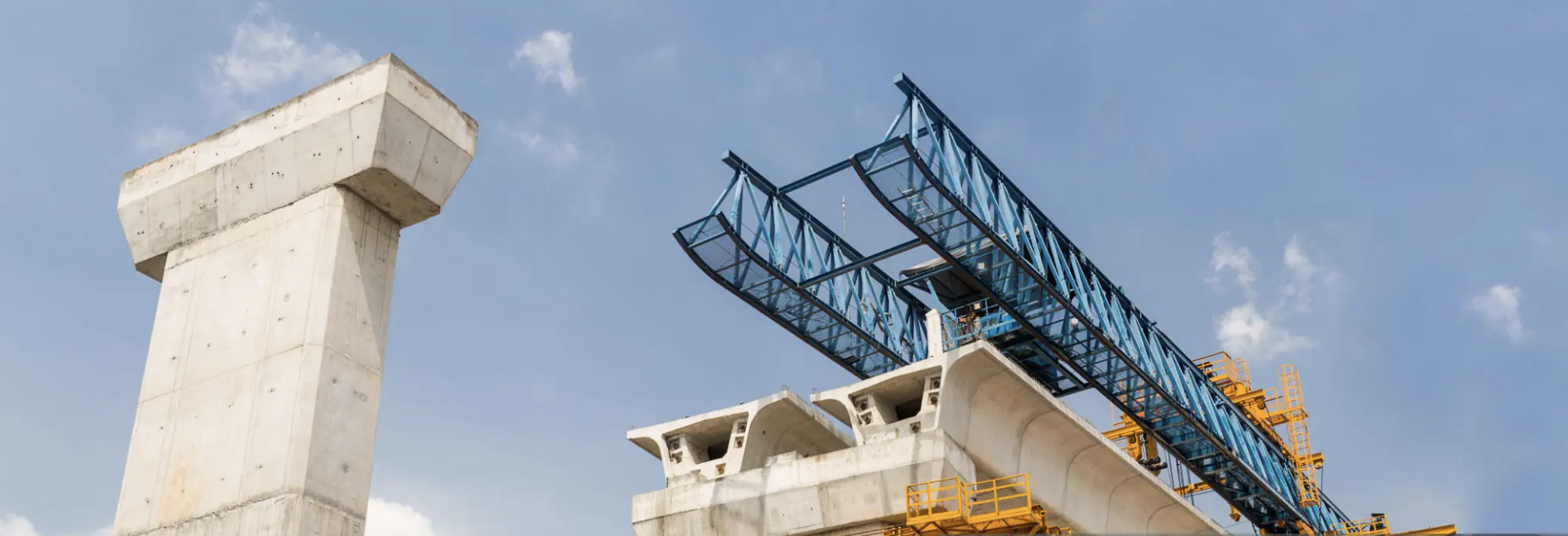 Bridge construction with concrete supports and a blue steel framework against a clear sky, representing large-scale infrastructure projects and high-yield real estate investments