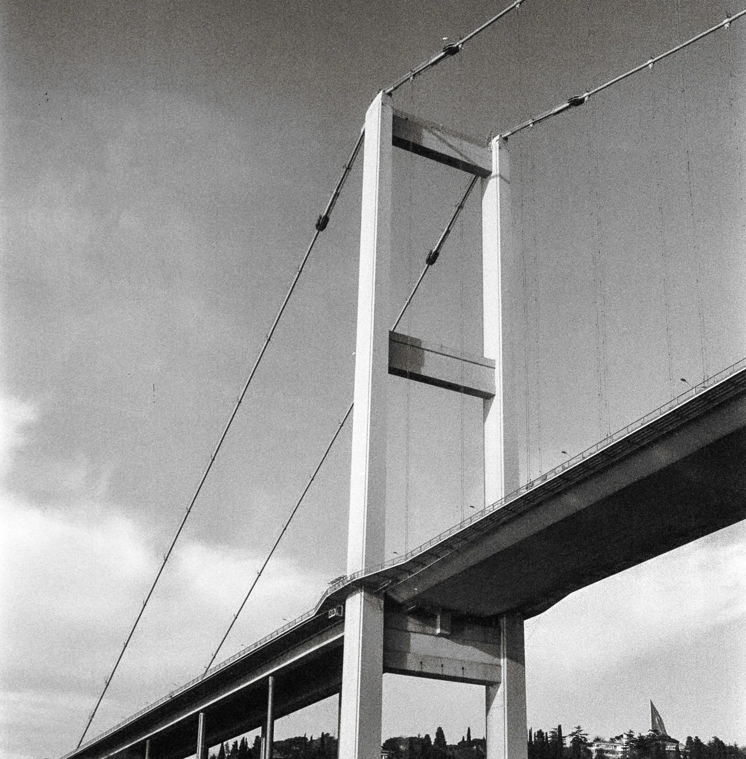 Black and white image of a modern suspension bridge with visible tower and cables, representing advanced infrastructure, engineering, and real estate investment opportunities.