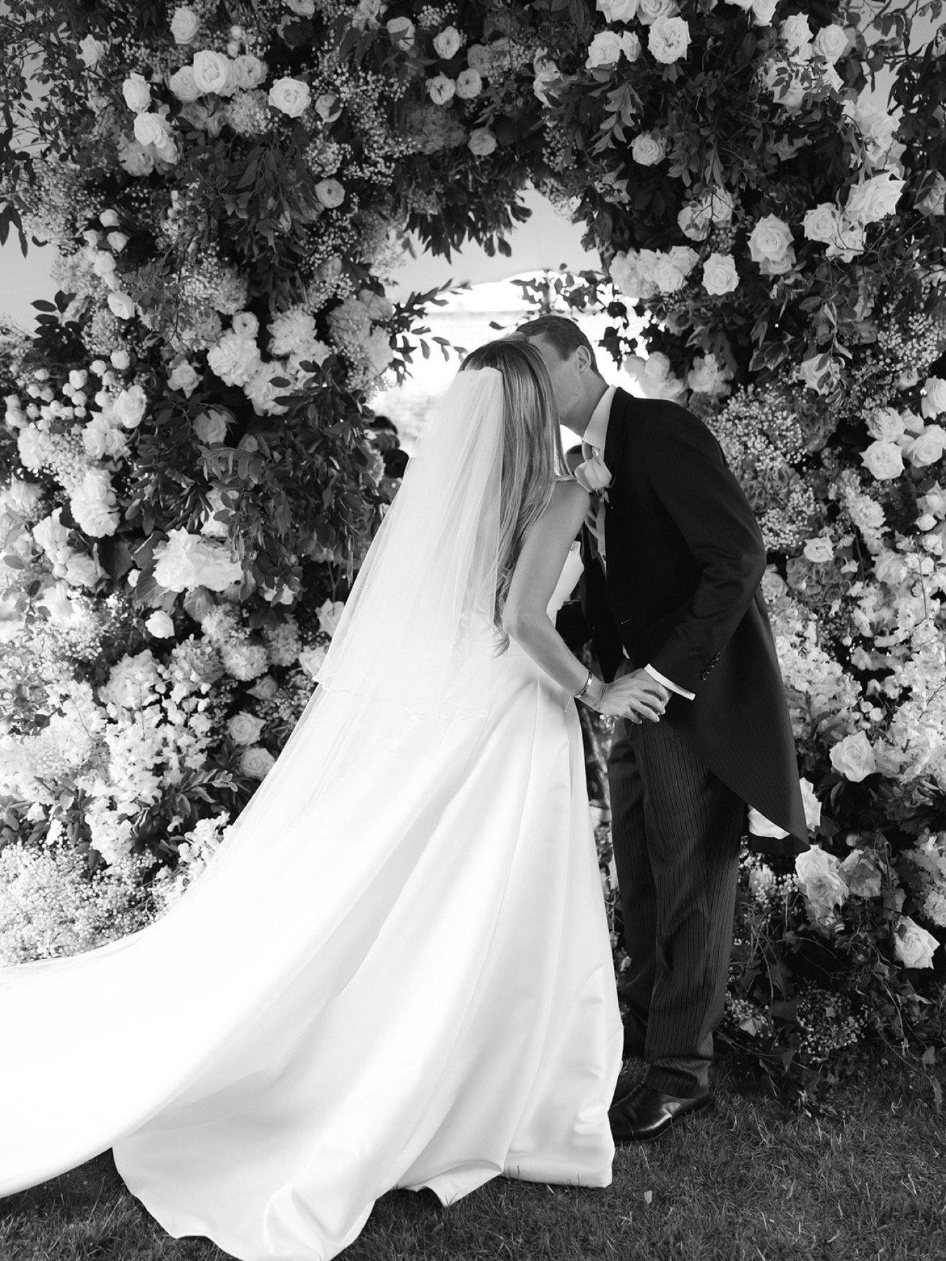 bride-groom-kissing-in-front-of-wedding-ceremony-arch-flowers.jpg