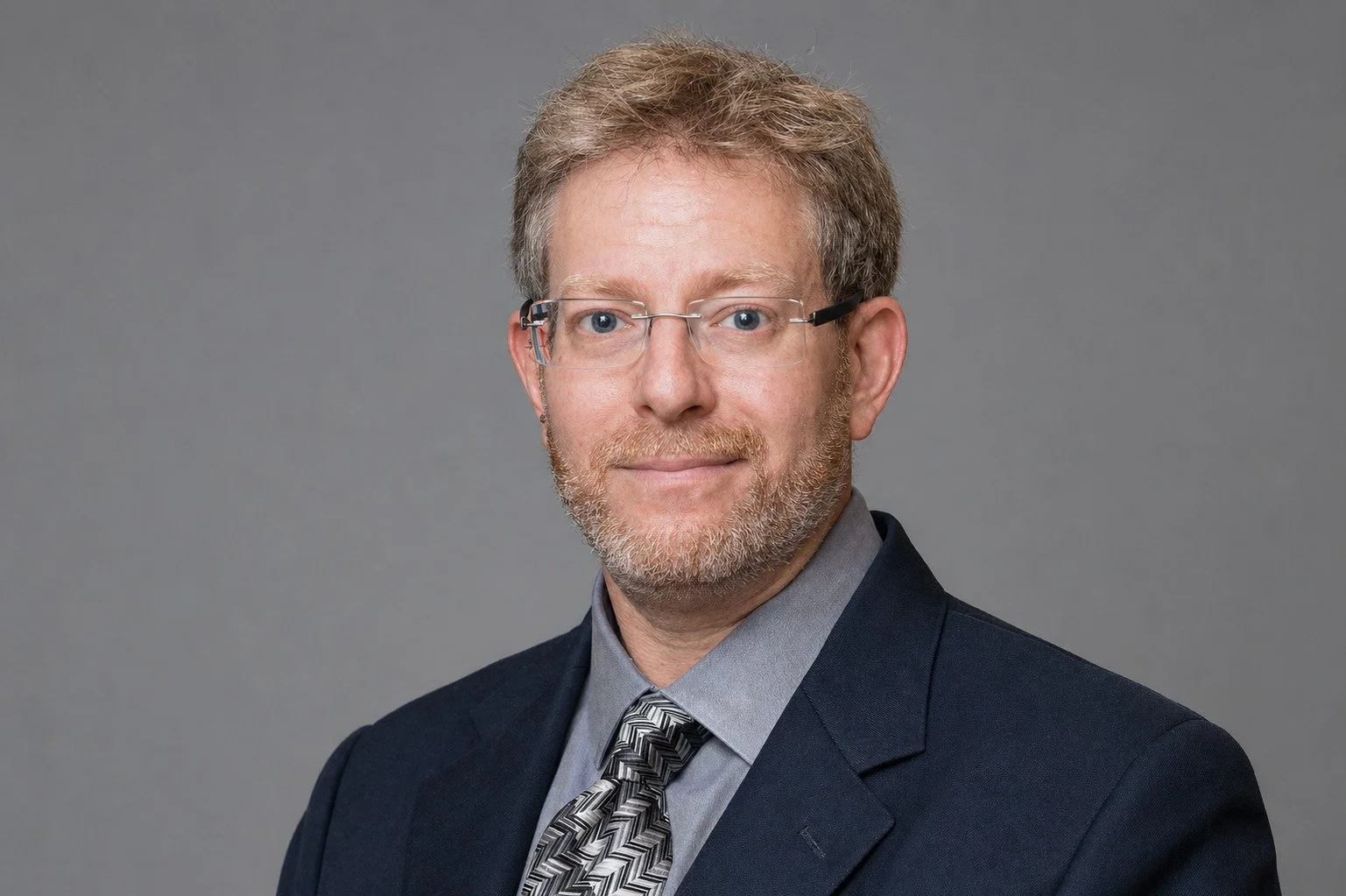 Professional headshot of Avram Joseph, Senior Counsel, Family Lawyer,  in suit, tie and glasses, on a grey background.