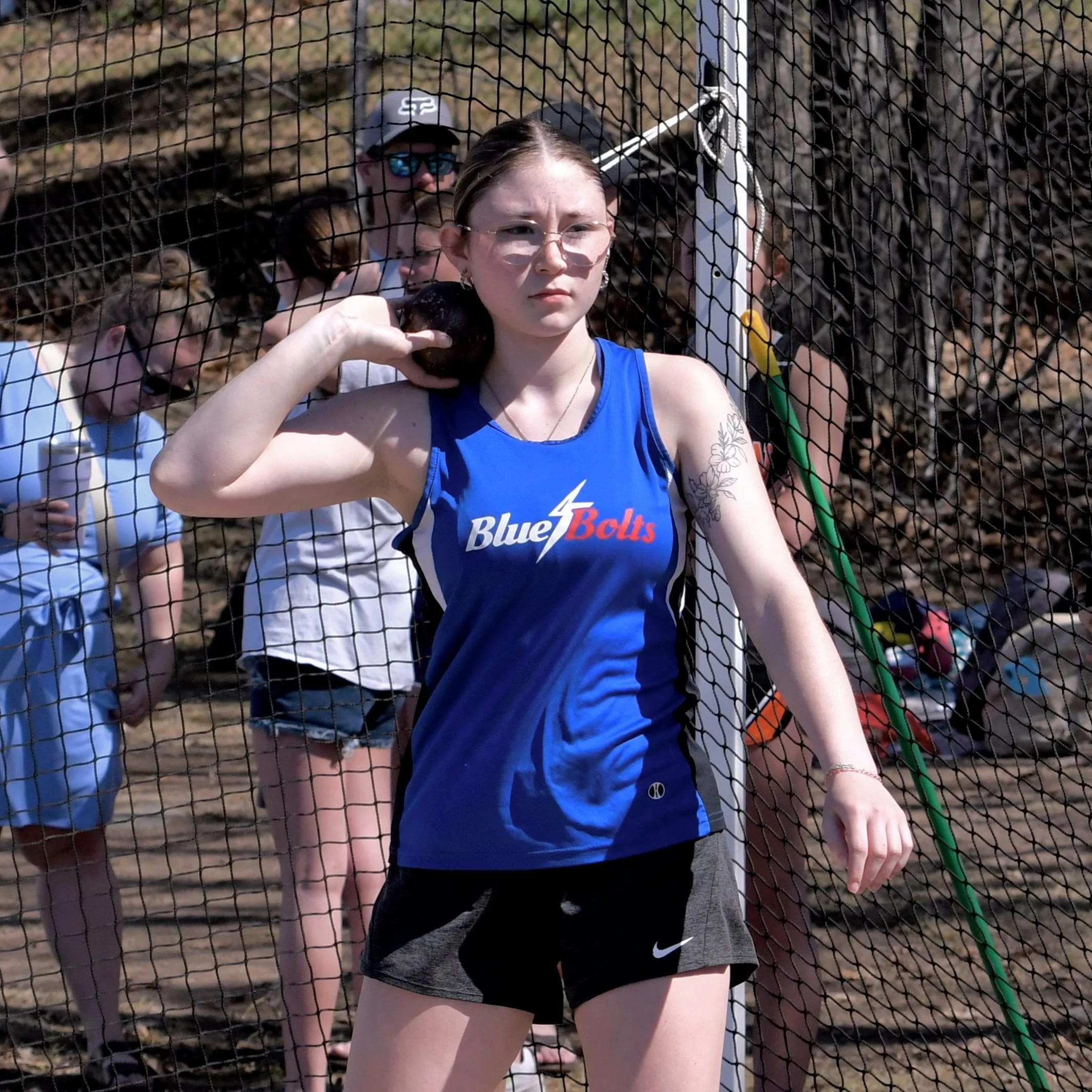 A high school female shot putter, concentrating, with the shot put by her ear just prior to the beginning of her throw.