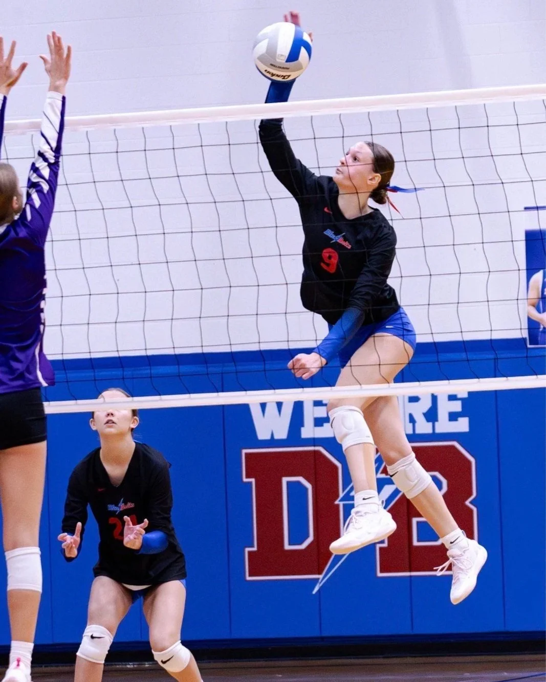 Dollar Bay volleyball player leaping above the net to spike a volleyball.