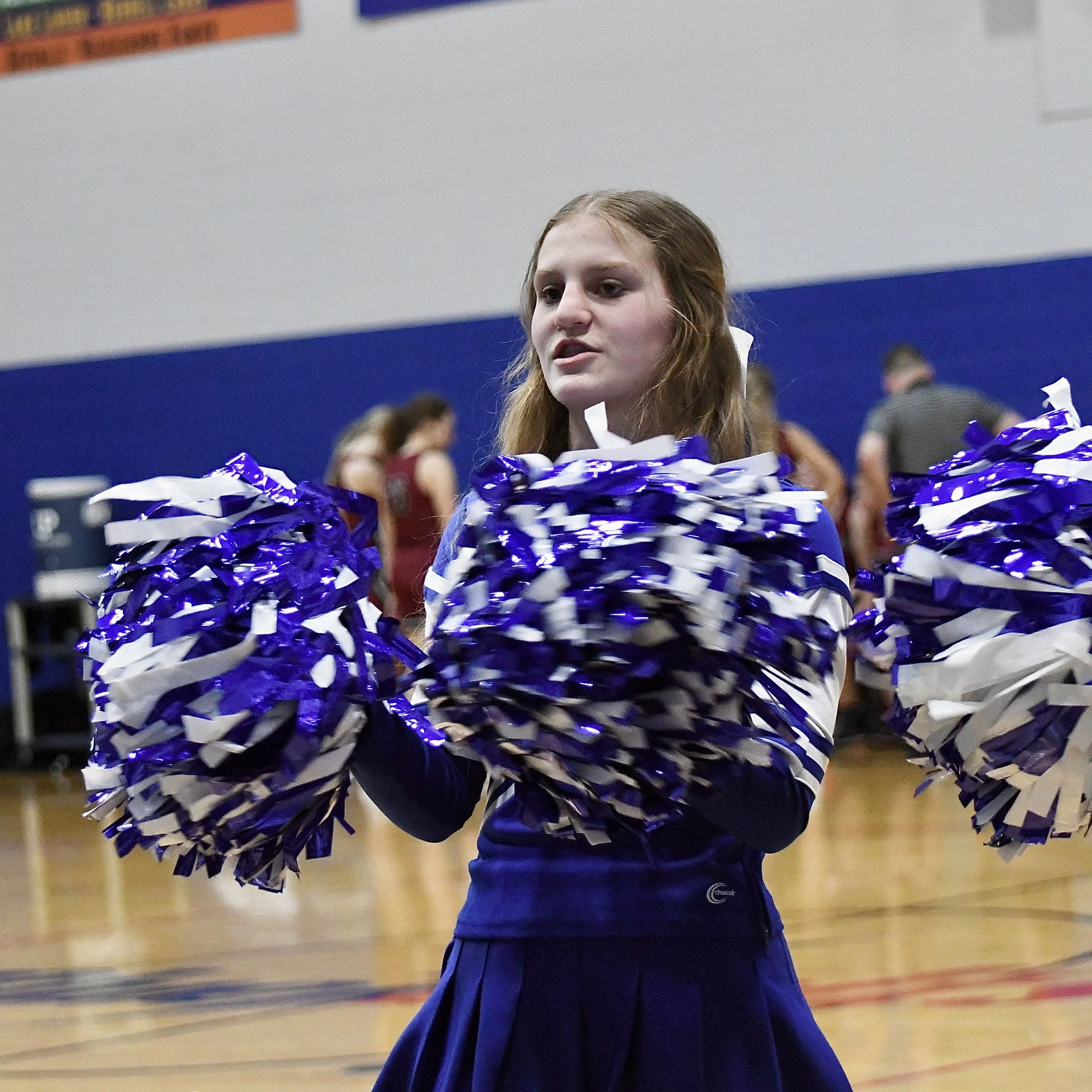 Close up of a varsity cheerleader with pom-poms in front of the fans., leading a cheer.