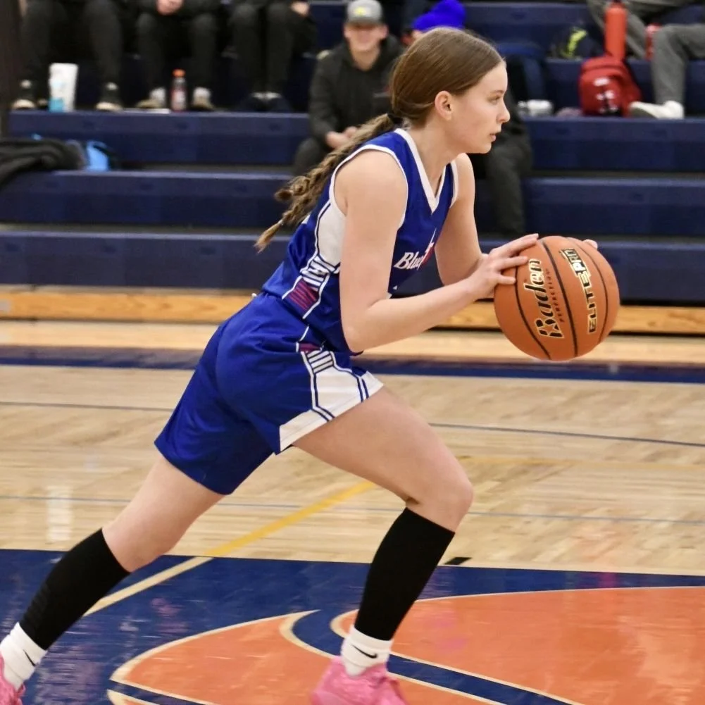 Varsity female stretched out while dribbling, quickly driving the ball towards from the back court to the front court.