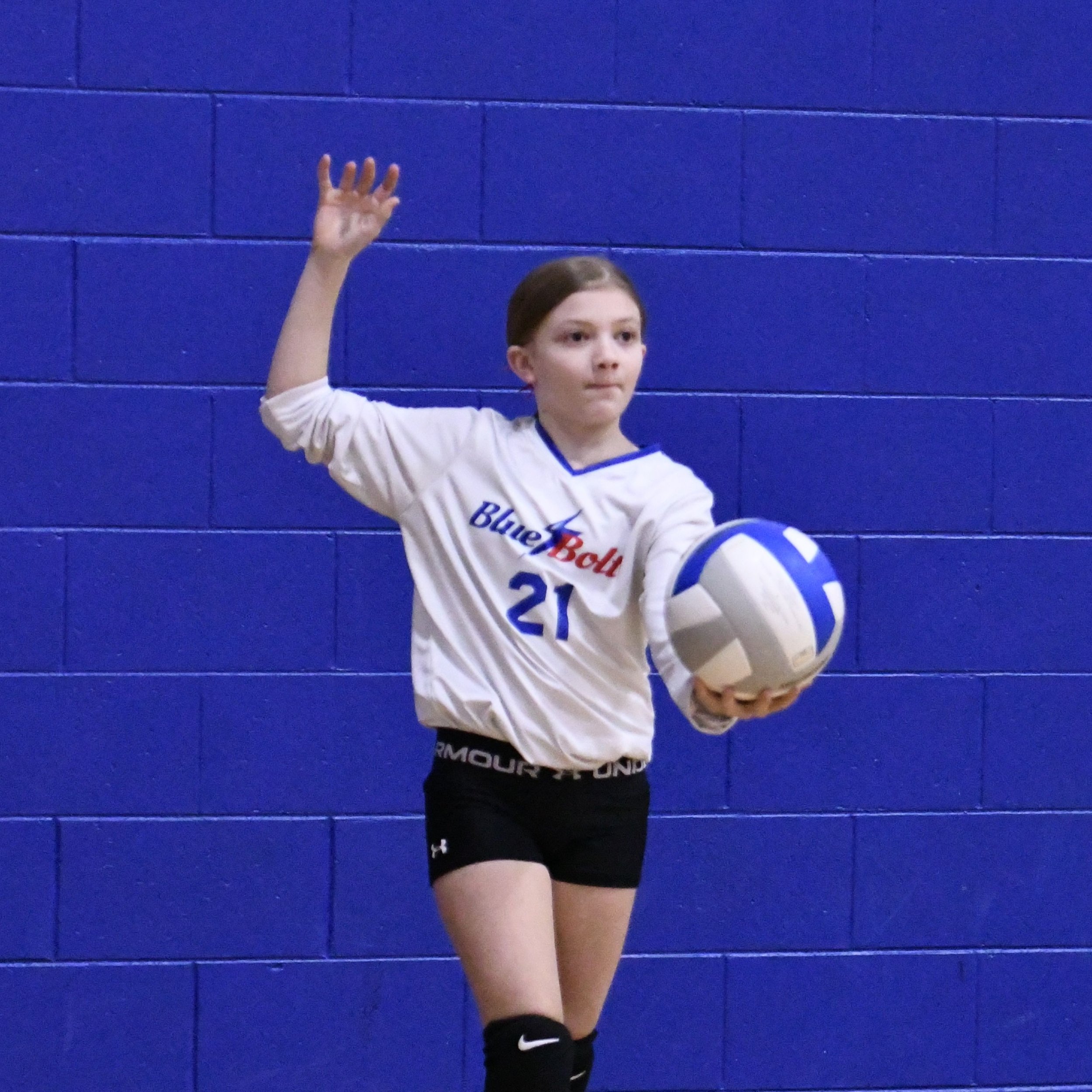 Junior Volleyball player in position to serve with arm raised above her head and the other arm extended holding the ball.