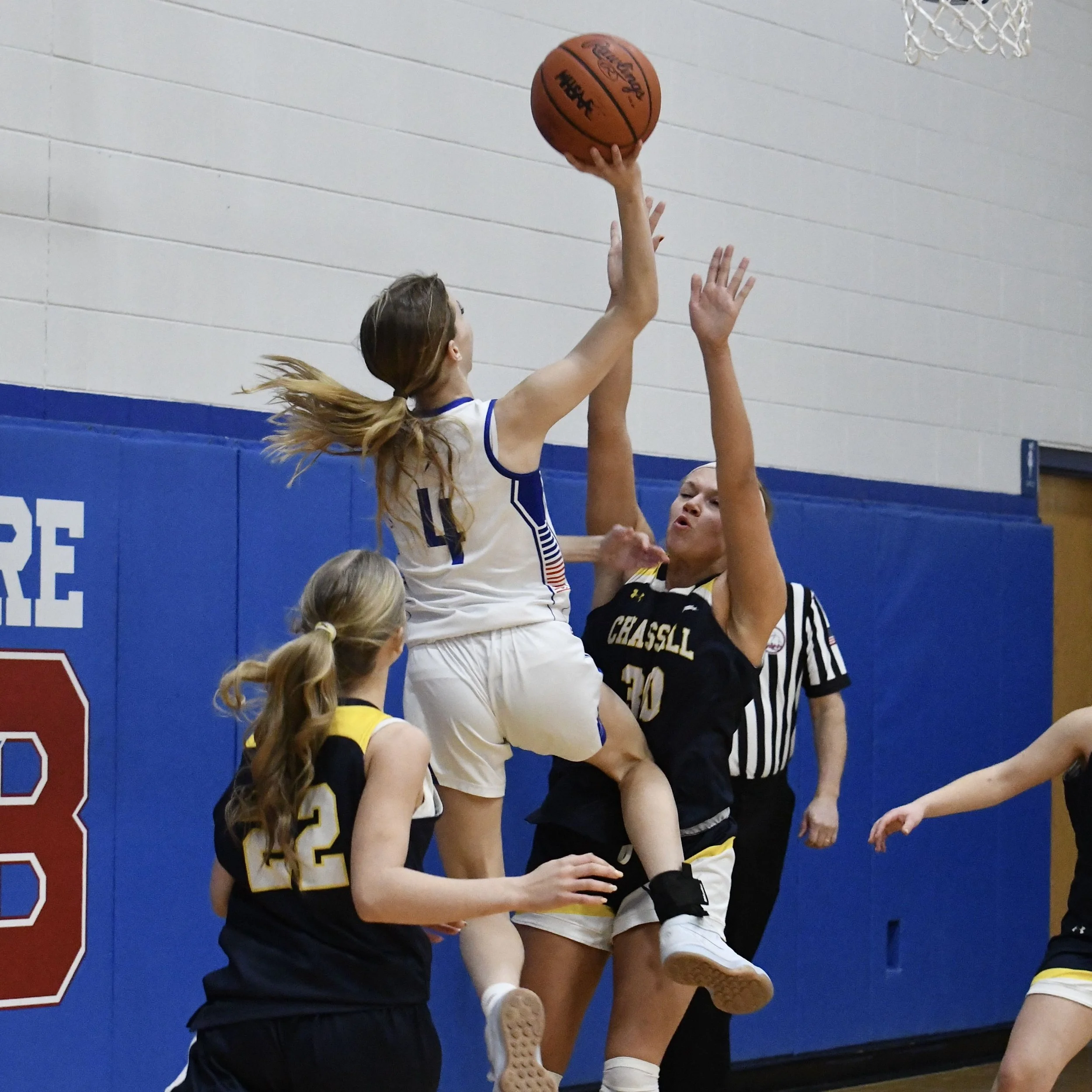 Varsity player rising over her opponent near the basket  to shoot a one hand layup.