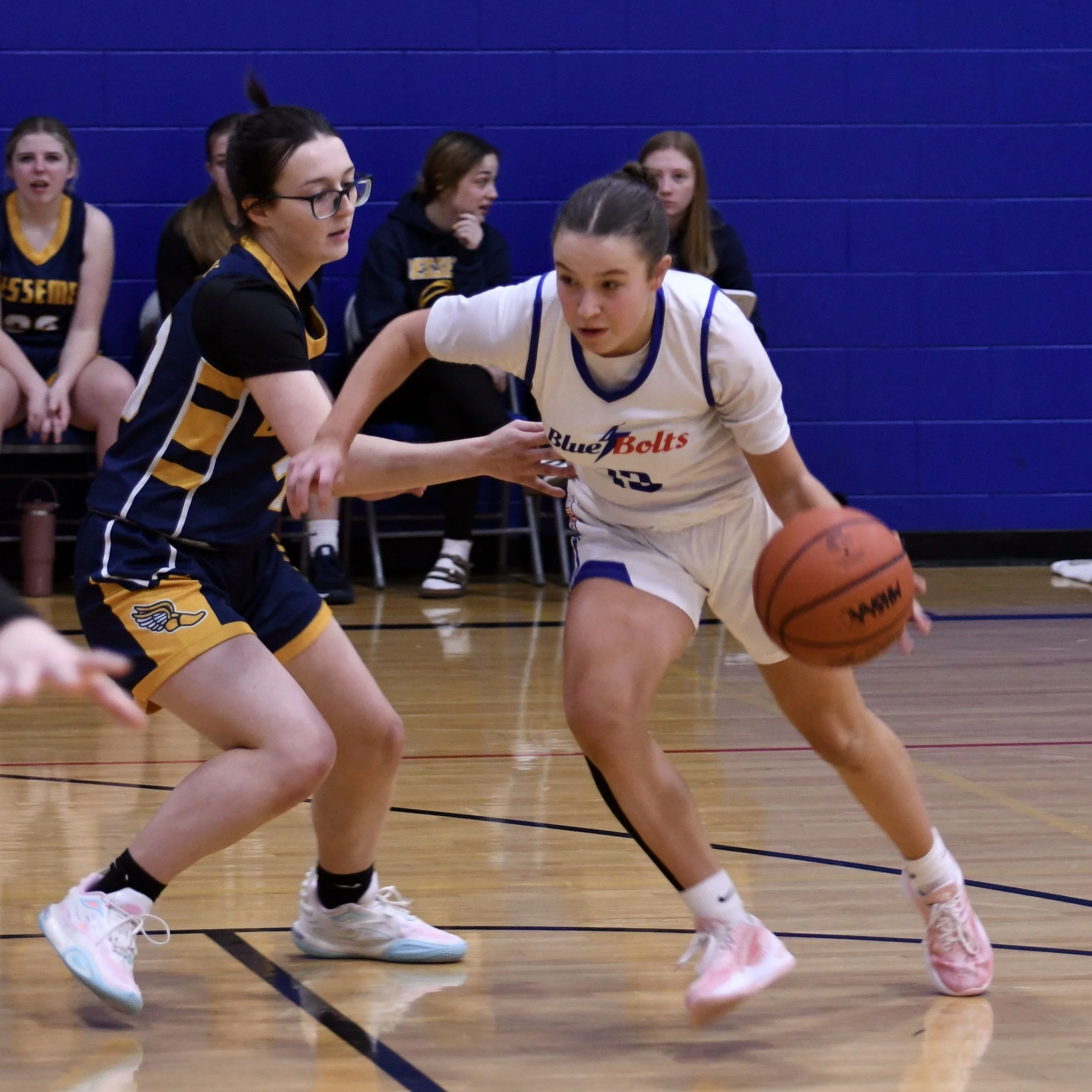 Varsity female lowering her shoulder, while trying to dribble past her defender at the top of the free-throw line.